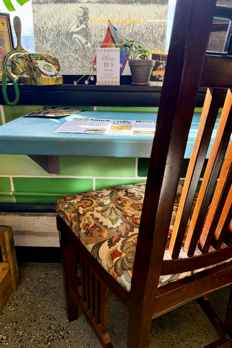 A wooden chair beside a window inside Urban Food Brood, with warm light and plants nearby.