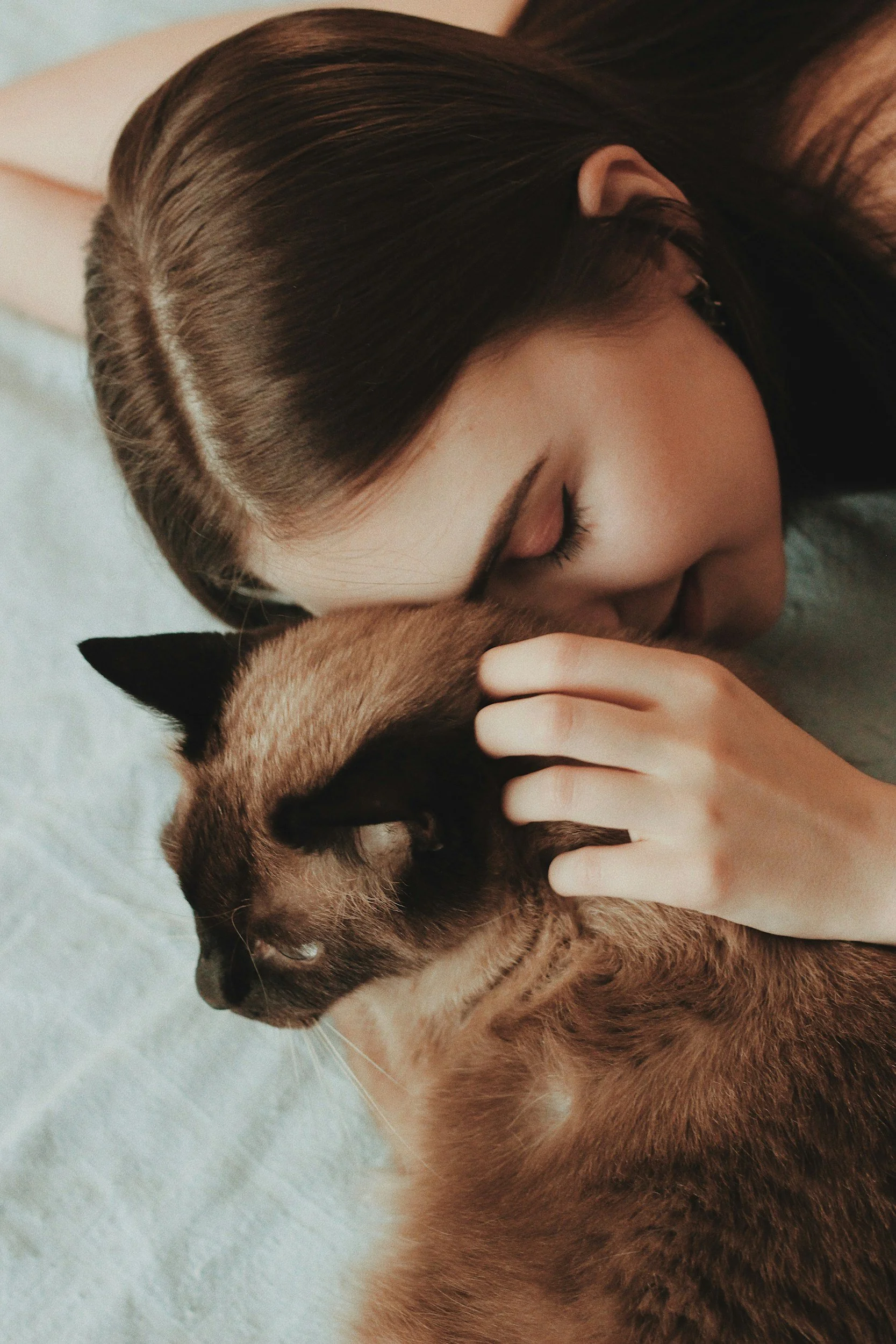 A person with brown hair lying on a white surface, cuddling a brown and black striped cat.