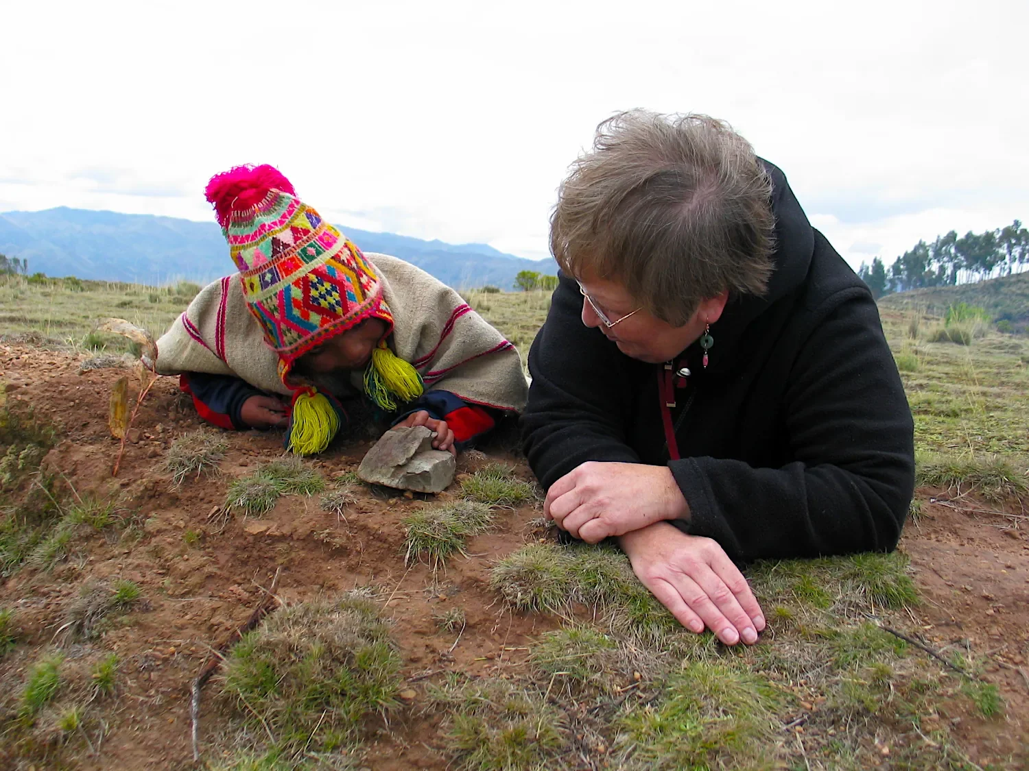 Q'ero child in the Peruvian Andes playing with a rock while a tourist watches