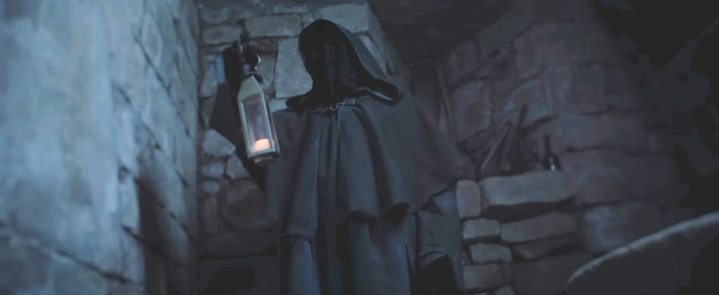 Une cape noire et un chapeau sont suspendus au mur en pierre, avec une lanterne allumée attachée à la muraille.
