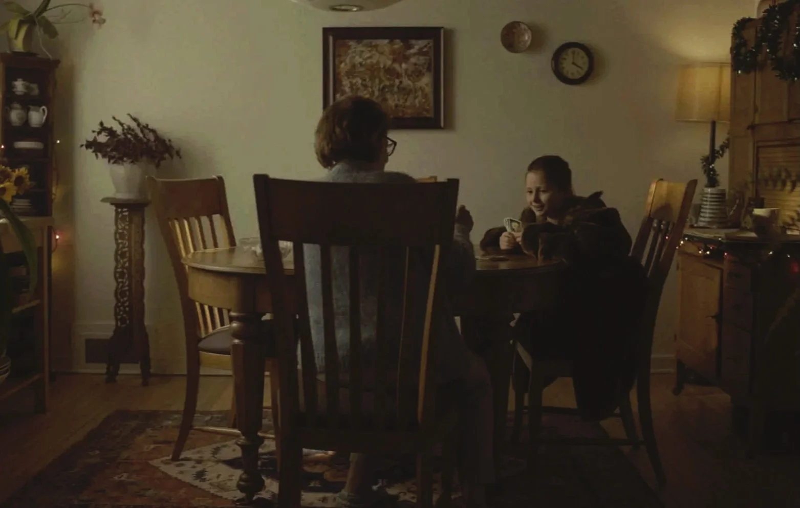 Une femme et un garçon assis à une table de cuisine, discutant ou jouant à des jeux de société dans une ambiance chaleureuse, avec des décorations de Noël.
