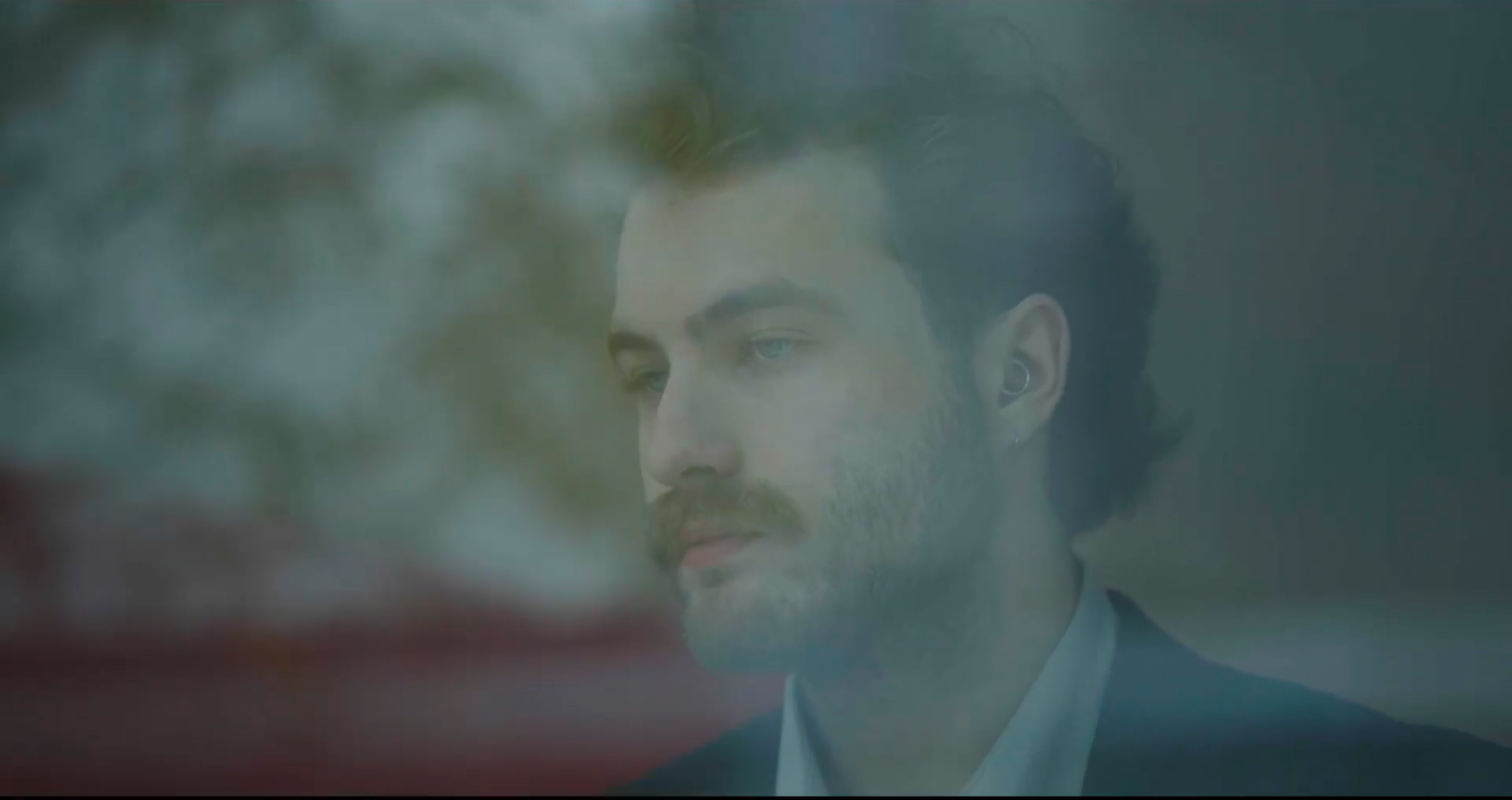 Homme avec barbe et boucle d'oreille, vu à travers une fenêtre floue.