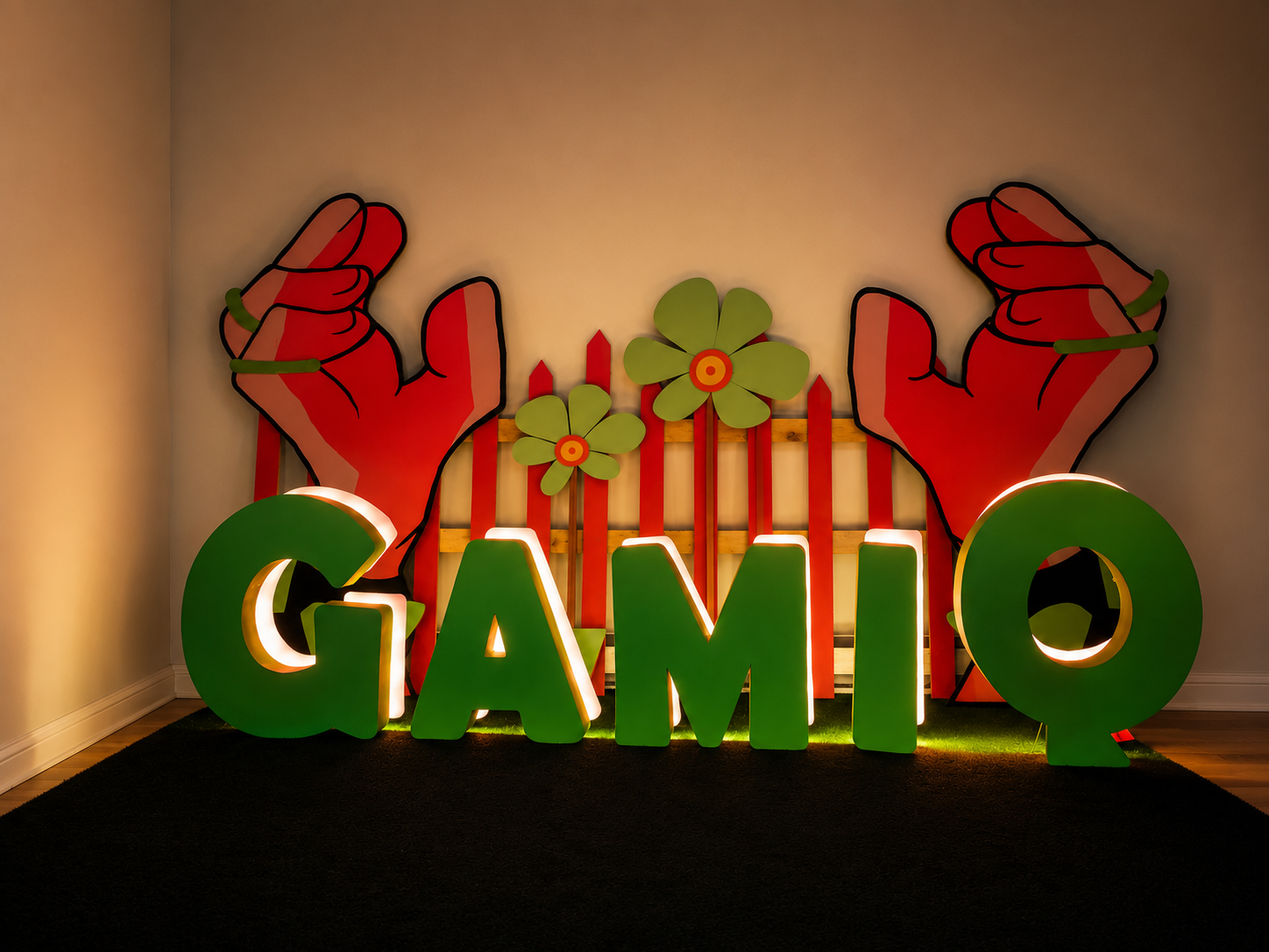 Décoration avec deux mains rouges stylisées, deux fleurs vertes et la phrase lumineuse "GAMIQ" en lettres vertes