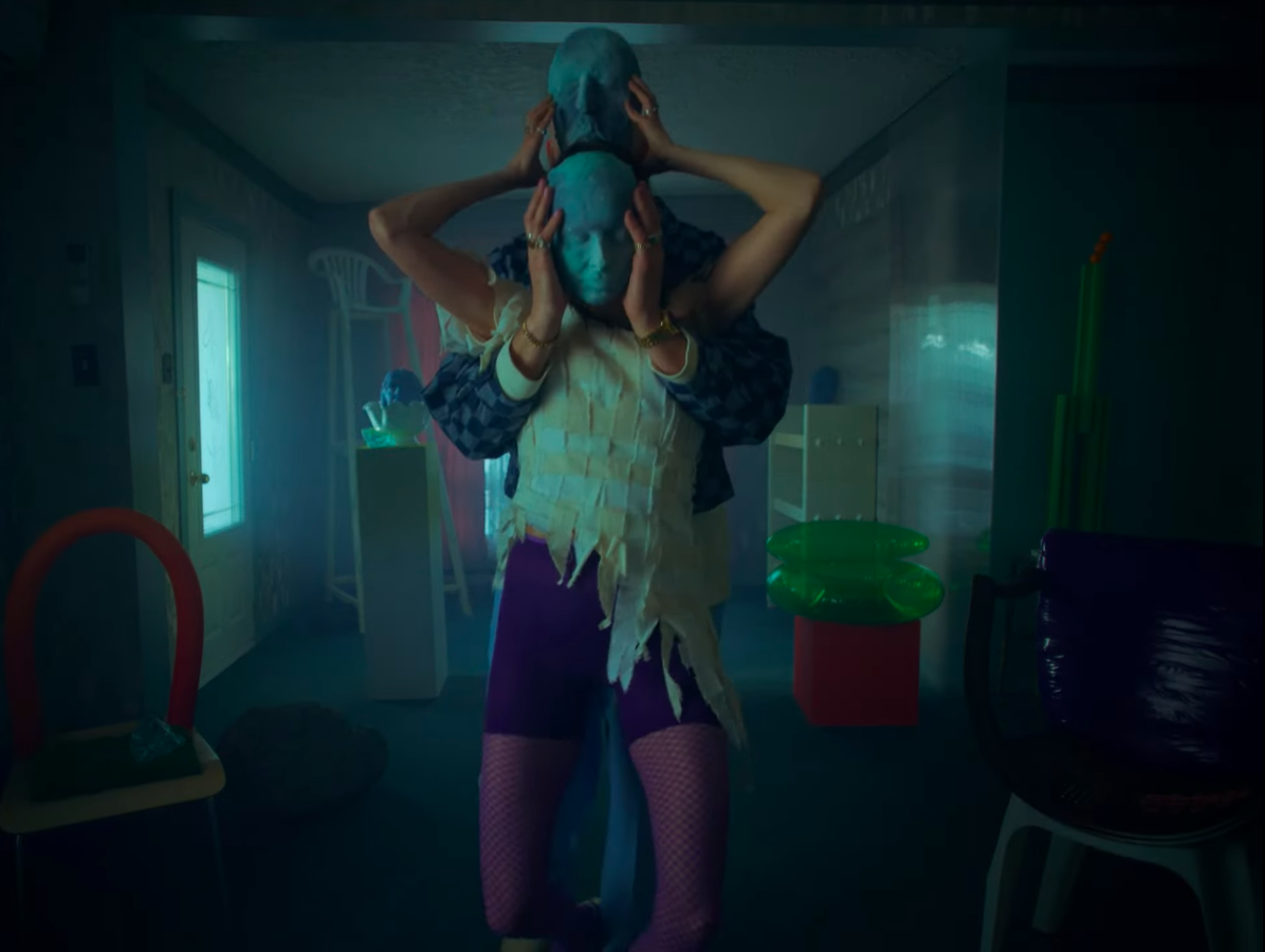 Personnes portant des masques dans une pièce sombre avec un mobilier coloré et un éclairage tamisé.