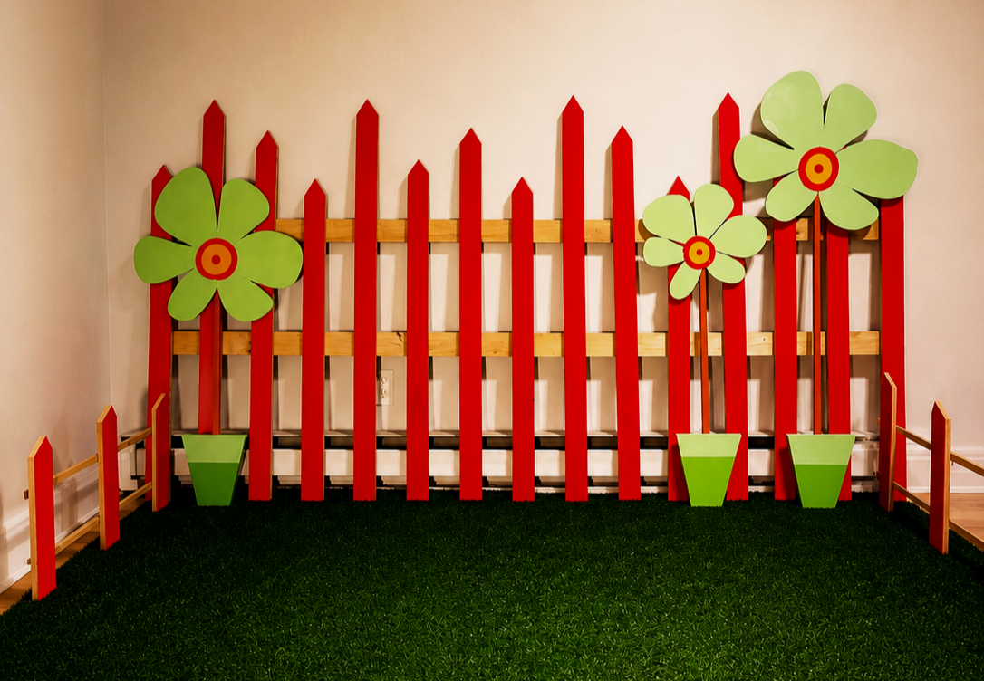 Décor de jardin avec des fleurs en bois vert et rouge, installation sur un mur beige avec pelouse artificielle au sol.