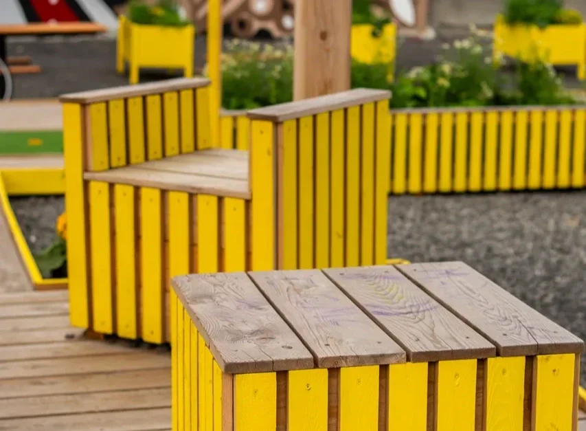 Mobilier urbain en bois peint en jaune dans un espace extérieur, avec des bancs et des structures de décoration.
