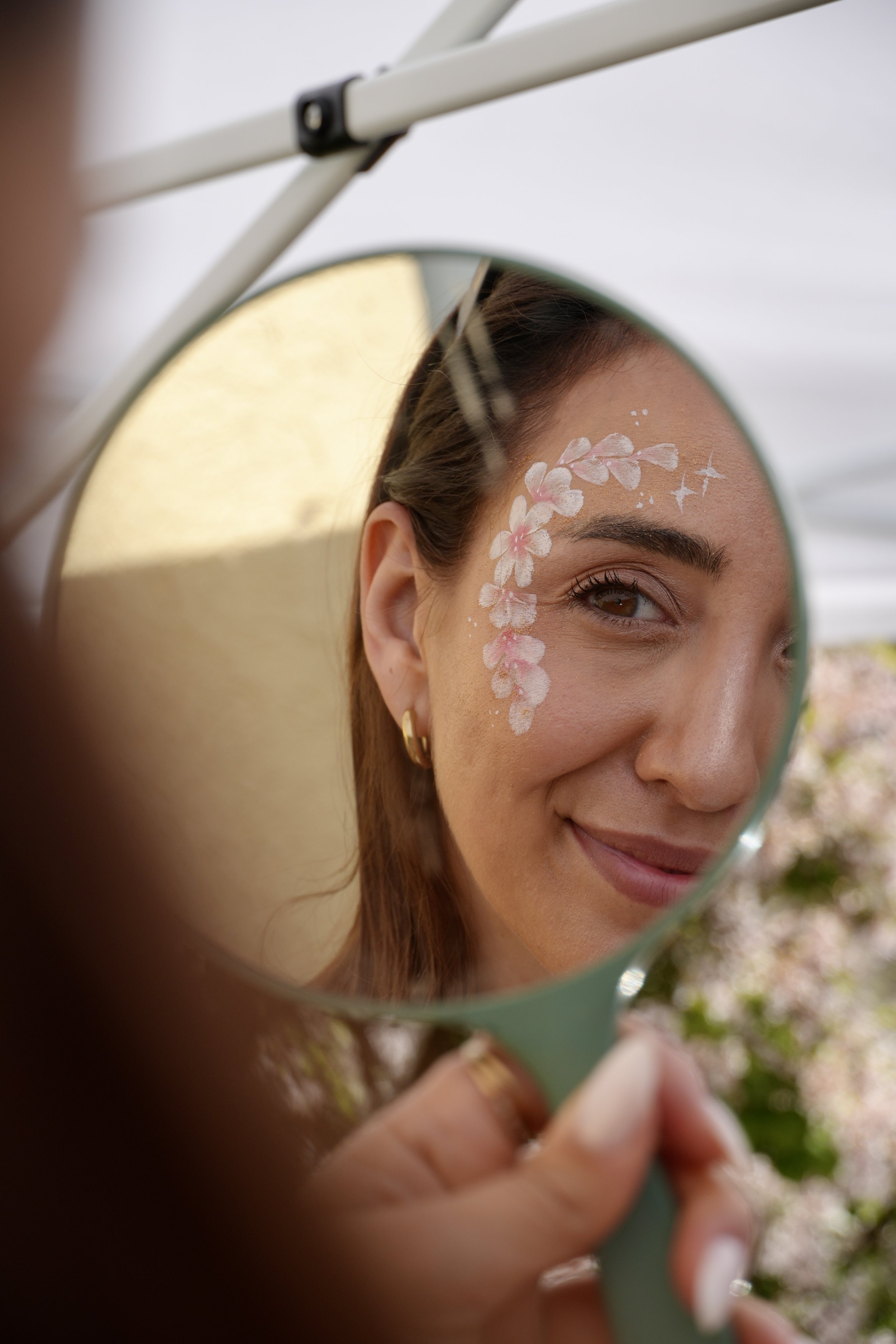 Nahaufnahme eines Gesichts im Spiegel mit Blumen-Make-up, bei Tageslicht, im Freien.