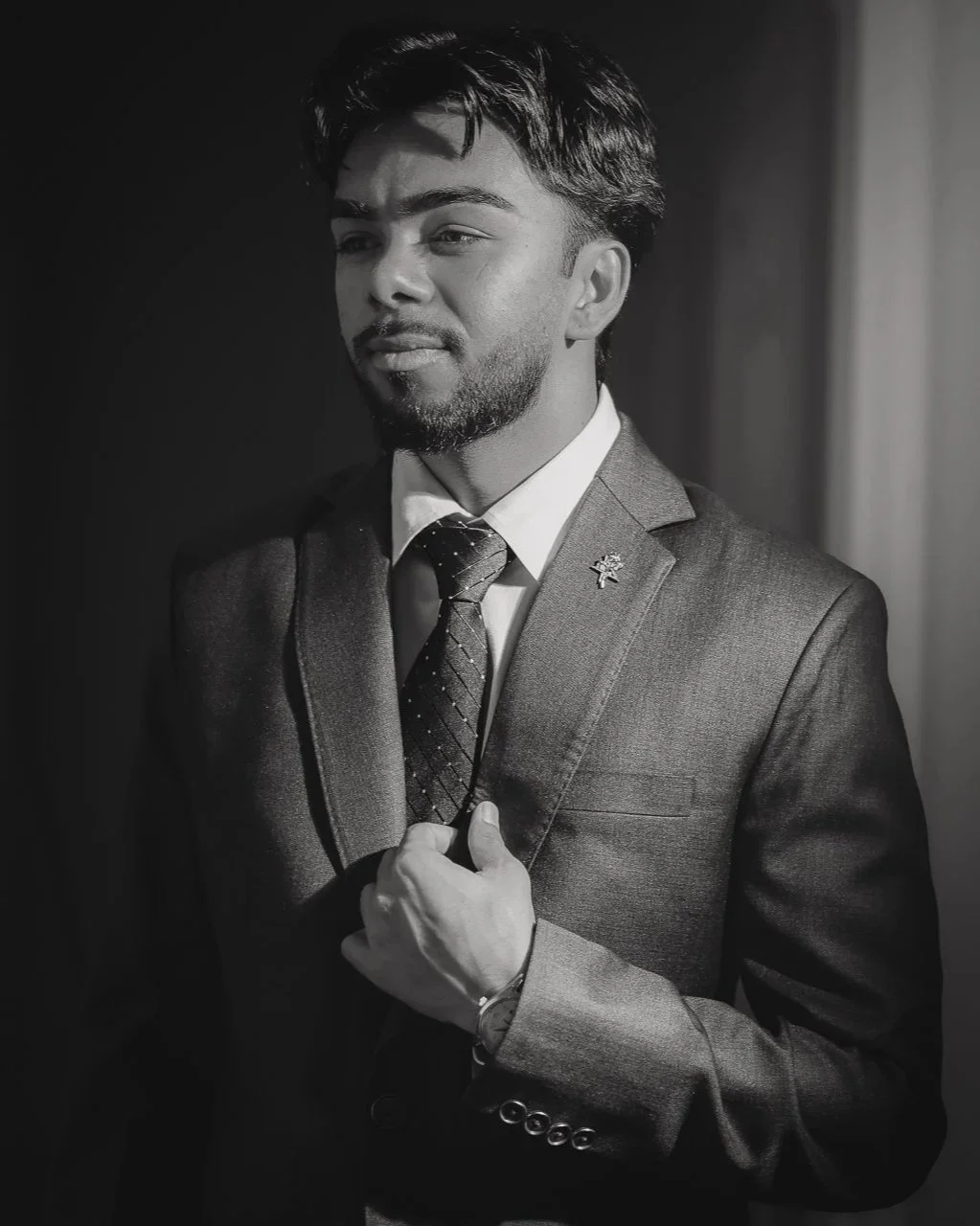 A black and white photo of a man in a suit, adjusting his tie, with a thoughtful expression.