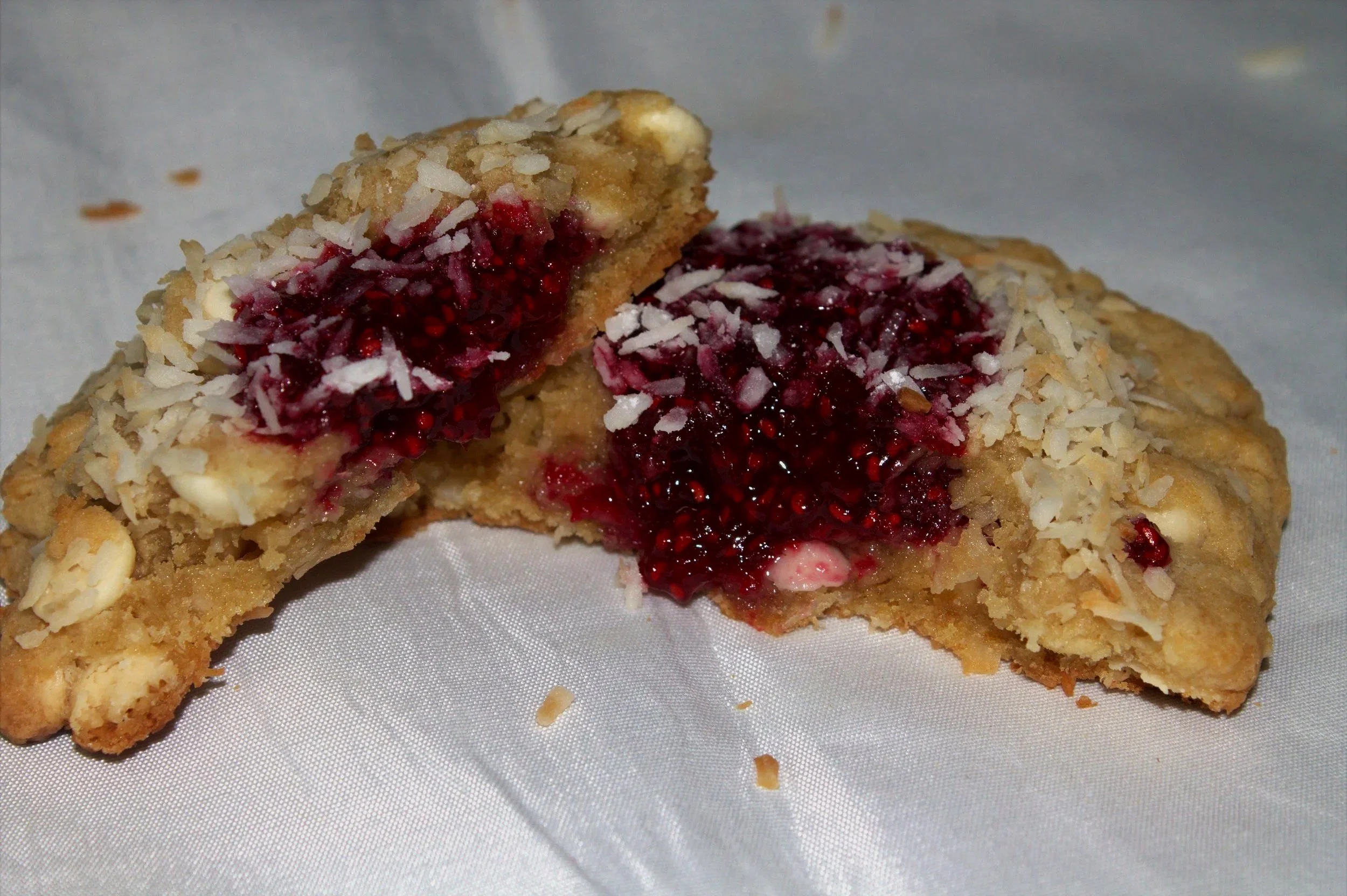Close-up of our raspberry filled coconut cookie, sprinkled with shredded coconut, on a white surface.