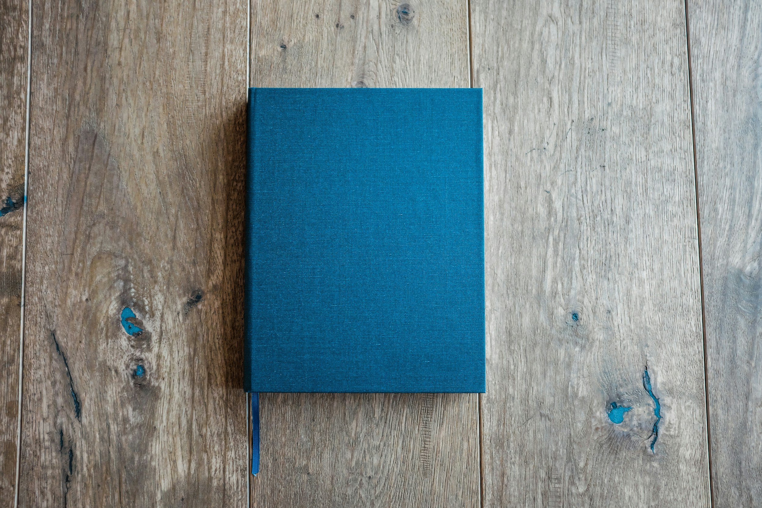 Blue hardcover book with a matching blue bookmark ribbon on a rustic wooden surface.