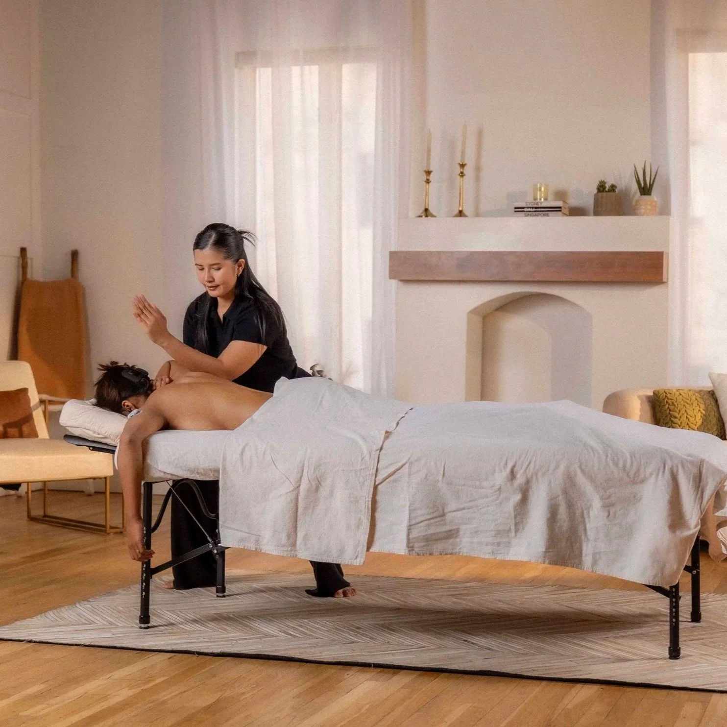 Licensed massage therapist using palm press technique on a client's upper back during a mobile table massage session at home
