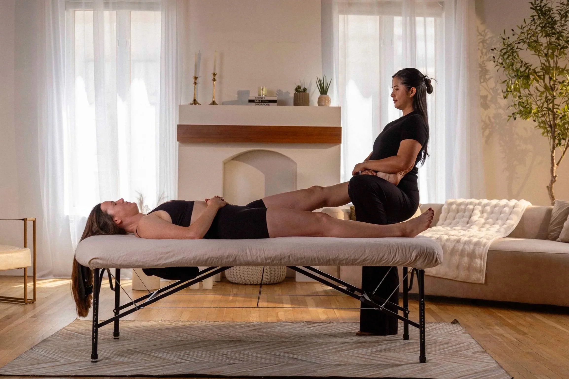 Sports massage therapist performing PNF leg stretching on a client lying on a portable massage table during an in-home athlete sports massage session