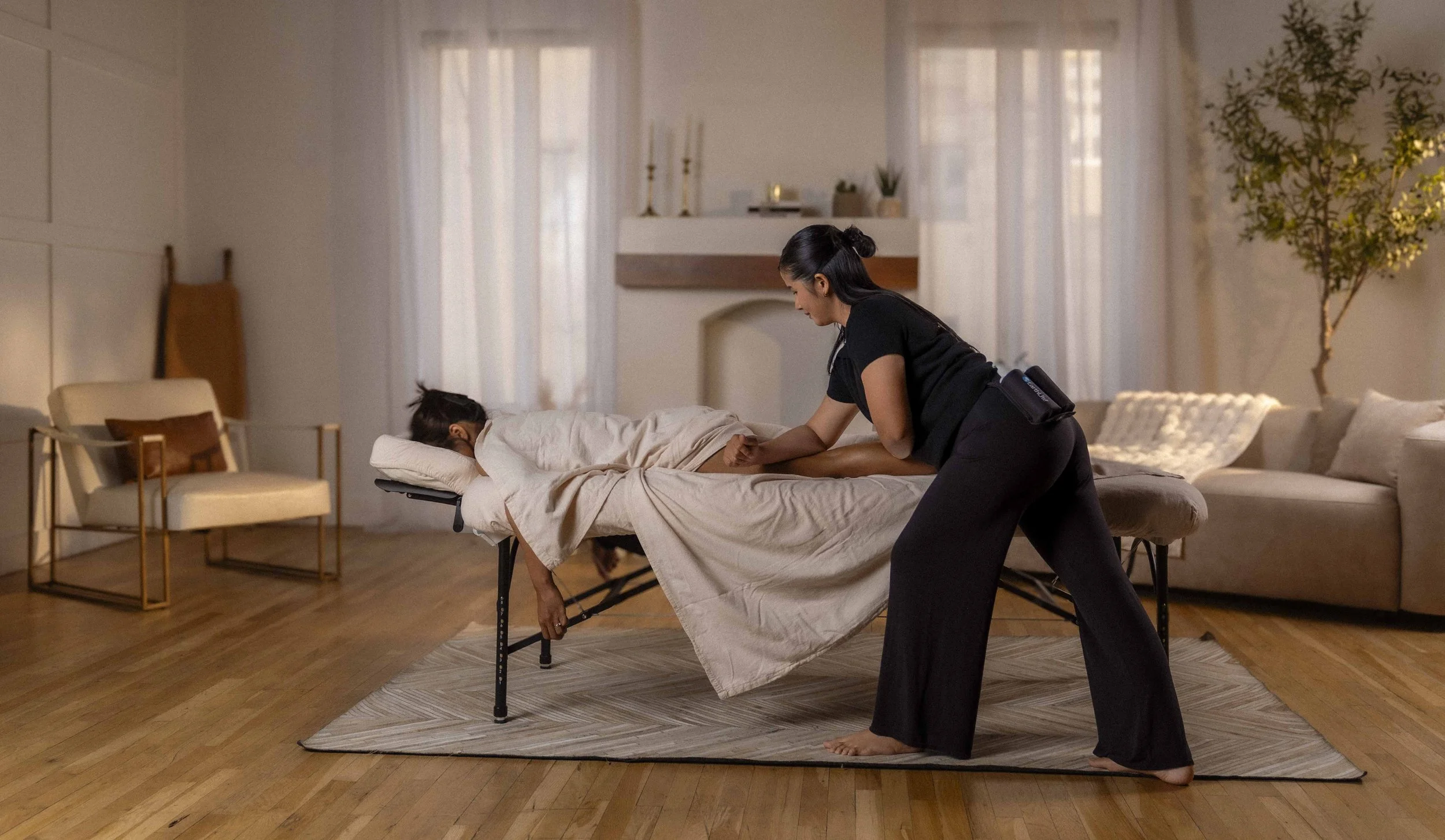 Mobile massage therapist performing deep tissue back massage on a client draped on a portable table during an in-home session