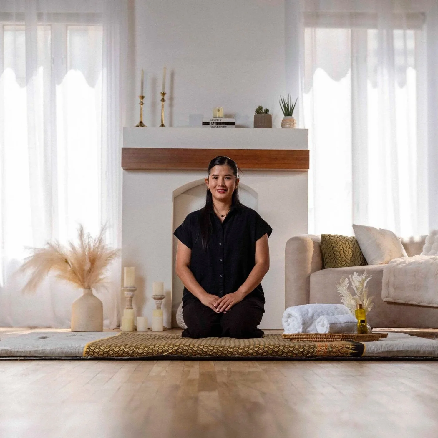 Mobile Thai massage therapist kneeling on a traditional mat in a client's home, ready to begin a session in Phoenix, AZ