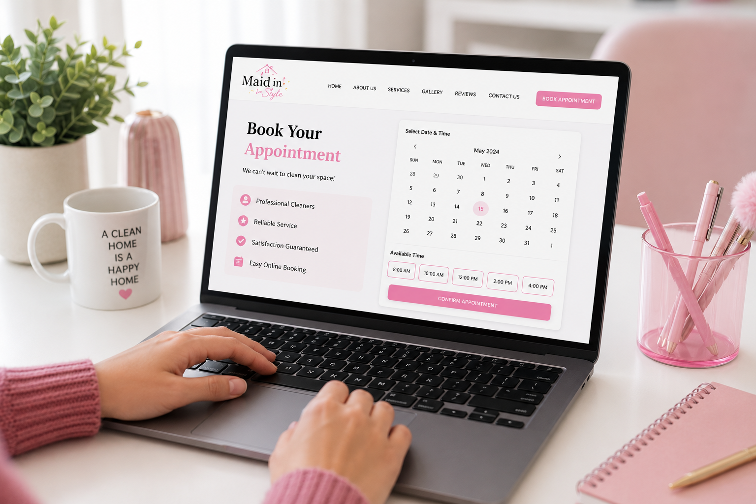 Laptop screen displaying an online booking page for a cleaning service with a calendar, available times, and a pink "Confirm Appointment" button. Surrounding items include a mug with cleaning slogan, pink pen holder with pens, pink notebook, and decorative plants.