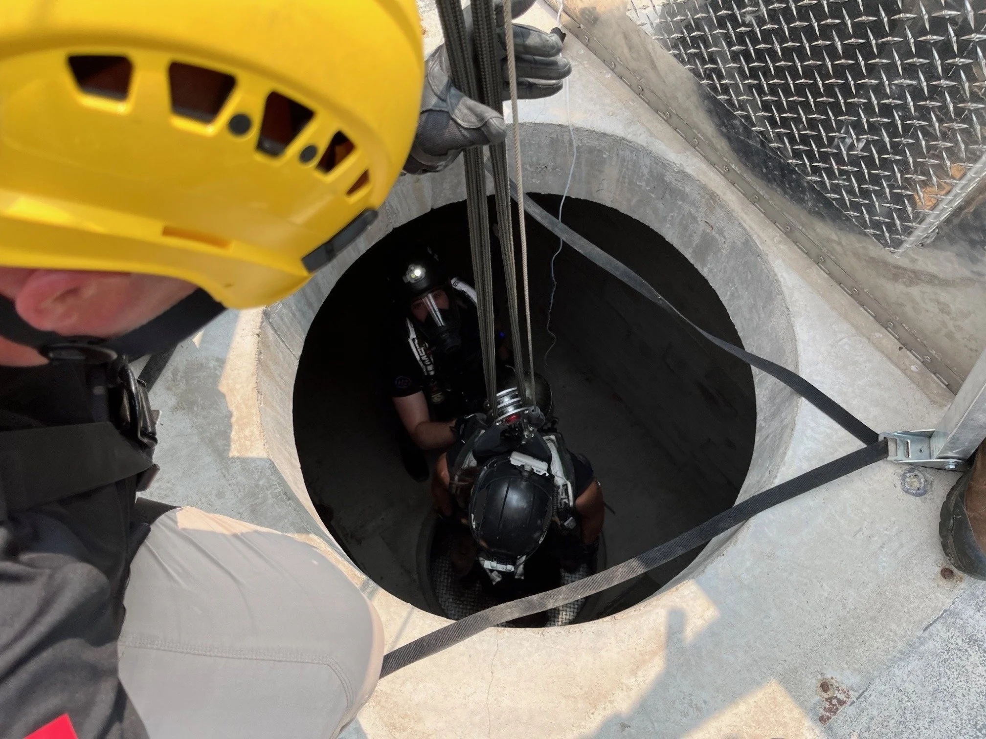 Worker wearing safety helmet and gloves using equipment to perform maintenance in an underground utility shaft.