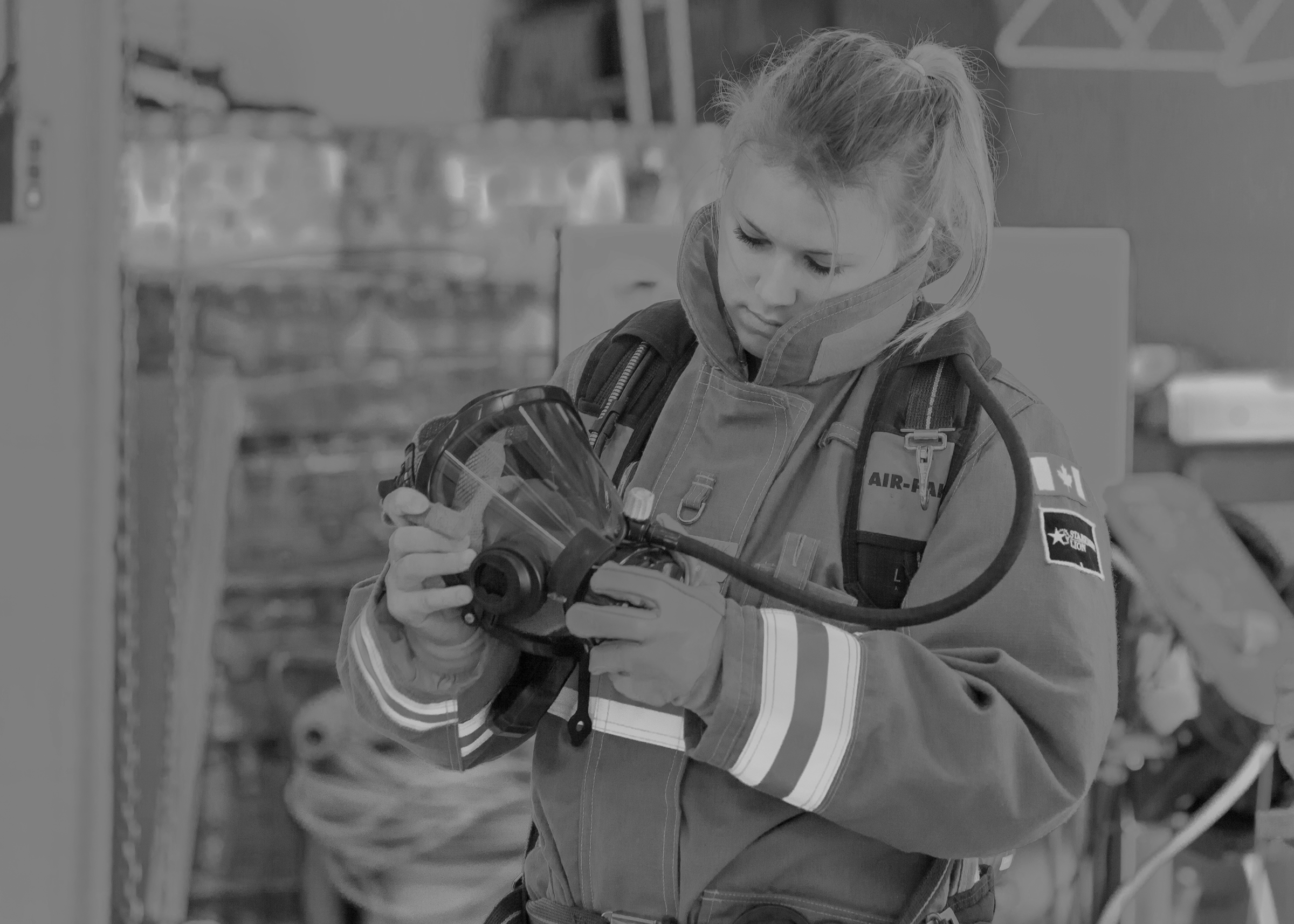 A young female firefighter in uniform inspecting a respirator Self Contained Breathing Apparatus or SCBA at her Fire Hall in preparation for her 2 year Respirator Fit Testing by Station 1 Safety and Rescue.