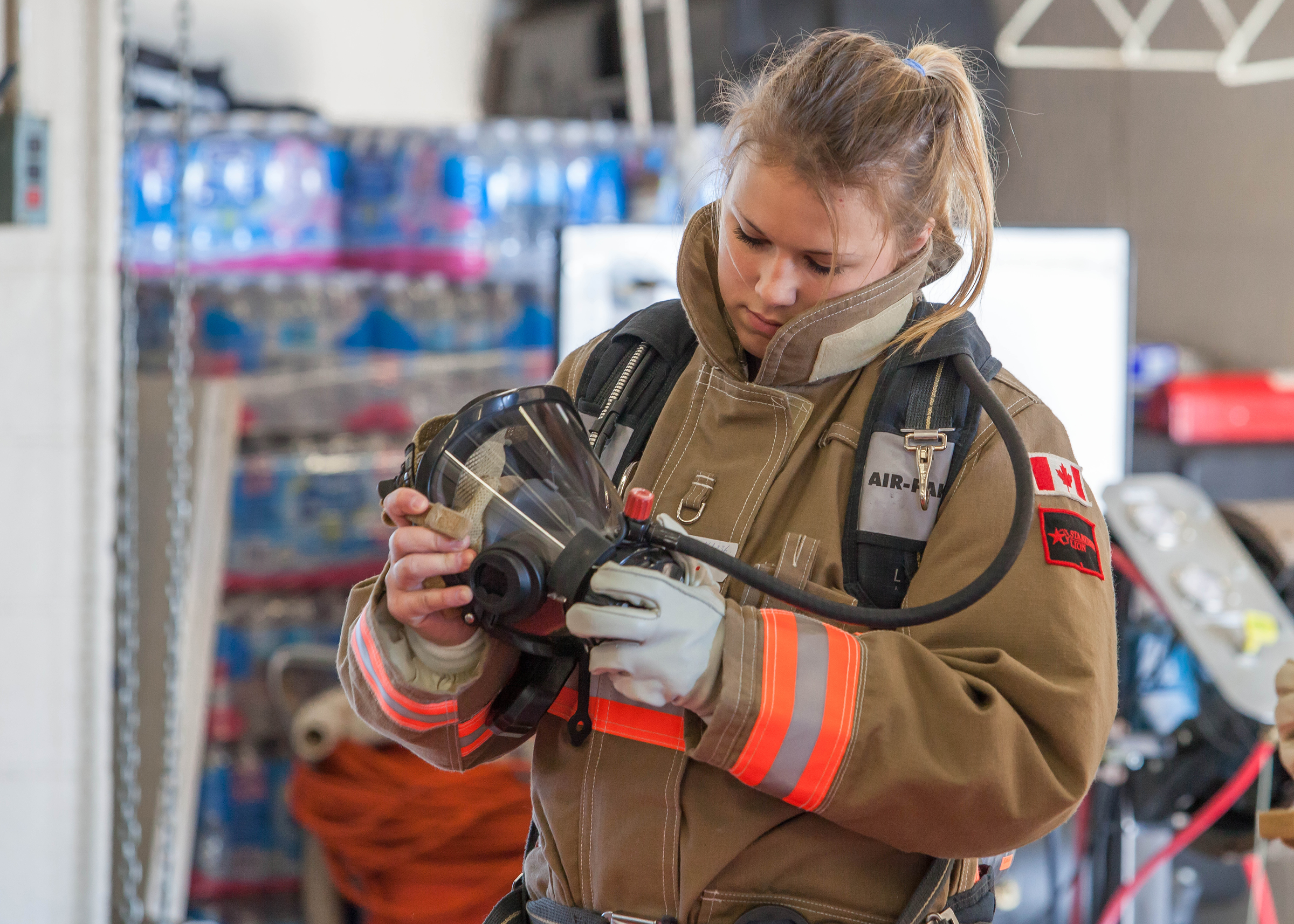 A young female firefighter in uniform inspecting a Self Contained Breathing Apparatus or SCBA at her Fire Hall in preparation for her 2 year Respirator Fit Testing by Station 1 Safety and Rescue.