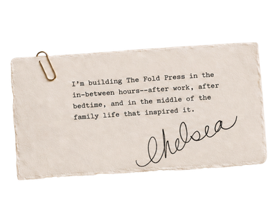 A handwritten note on a piece of paper that reads: "I'm building The Fold Press in the in-between hours—after work, after bedtime, and in the middle of the family life that inspired it." The note is secured to a surface with a gold paperclip.