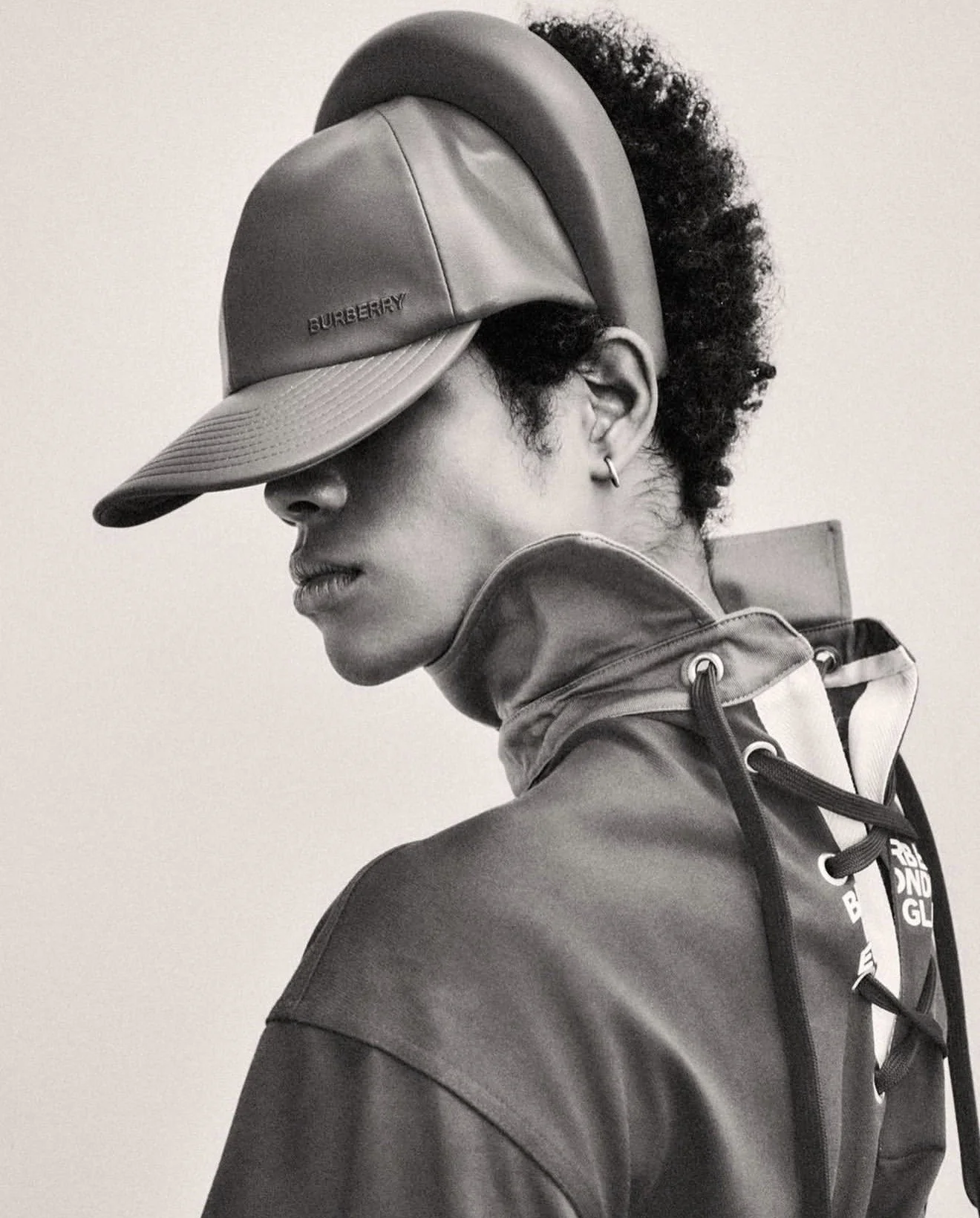JACOB RUTLEDGE in Black and white photo of a person with curly hair wearing a cap and jacket, facing sideways with eyes closed, in front of a plain background.