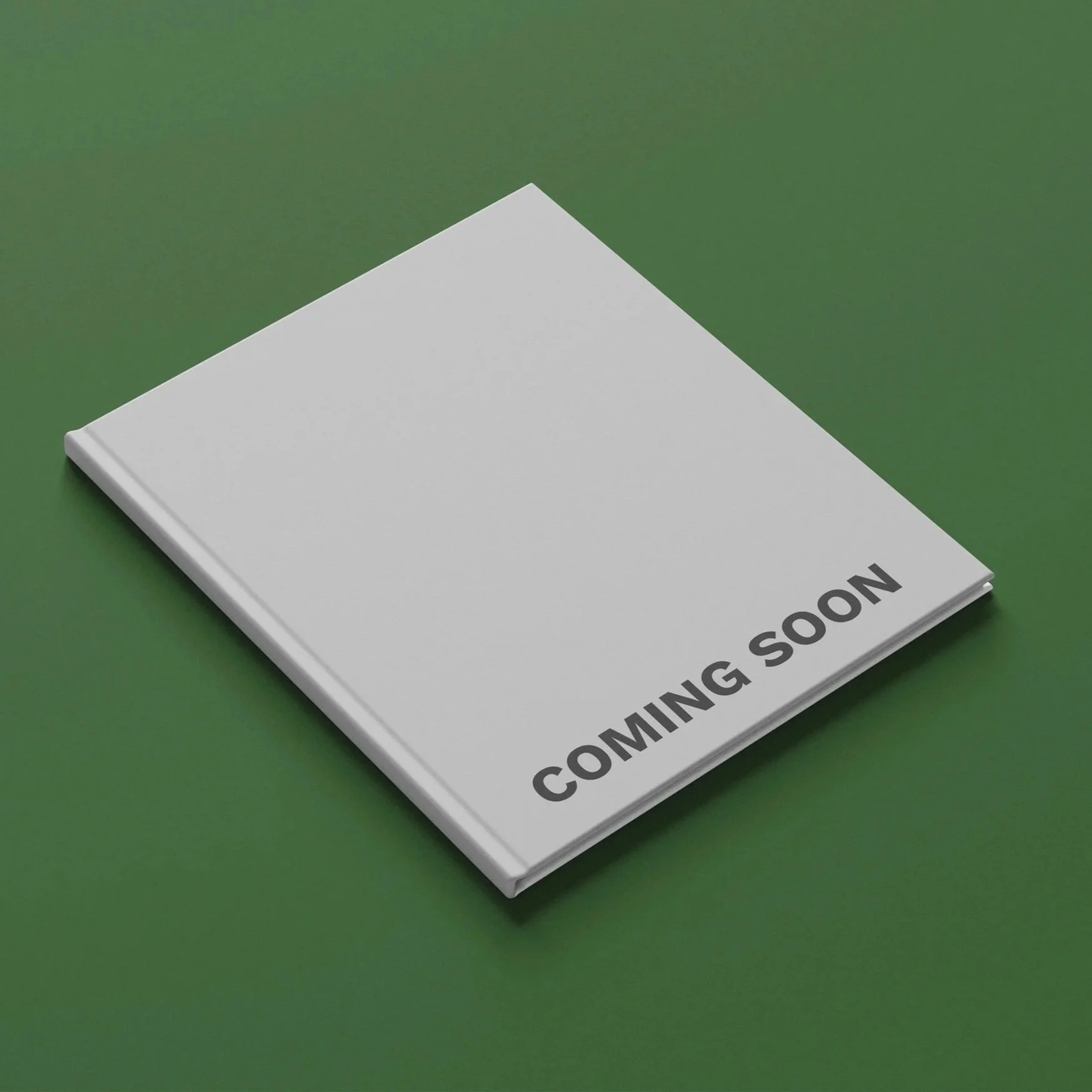 A grey book mockup with the words 'COMING SOON' written in black on the cover, placed on a green surface.