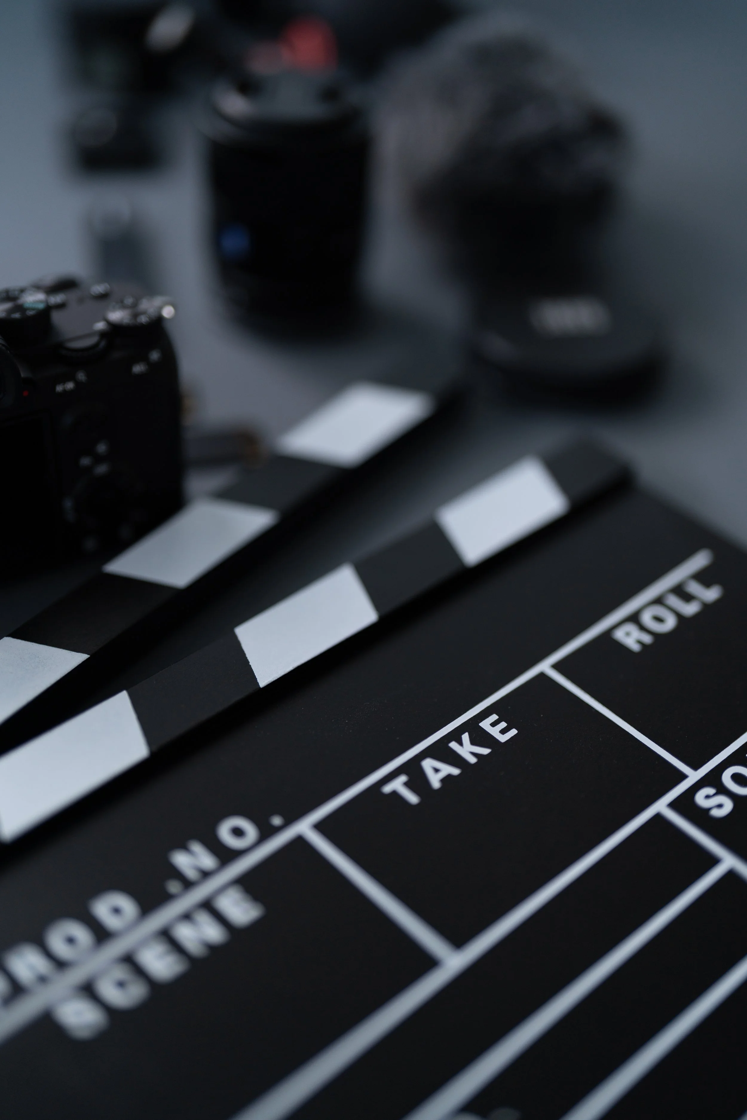 Close-up of a film clapboard with blurred camera equipment in the background.
