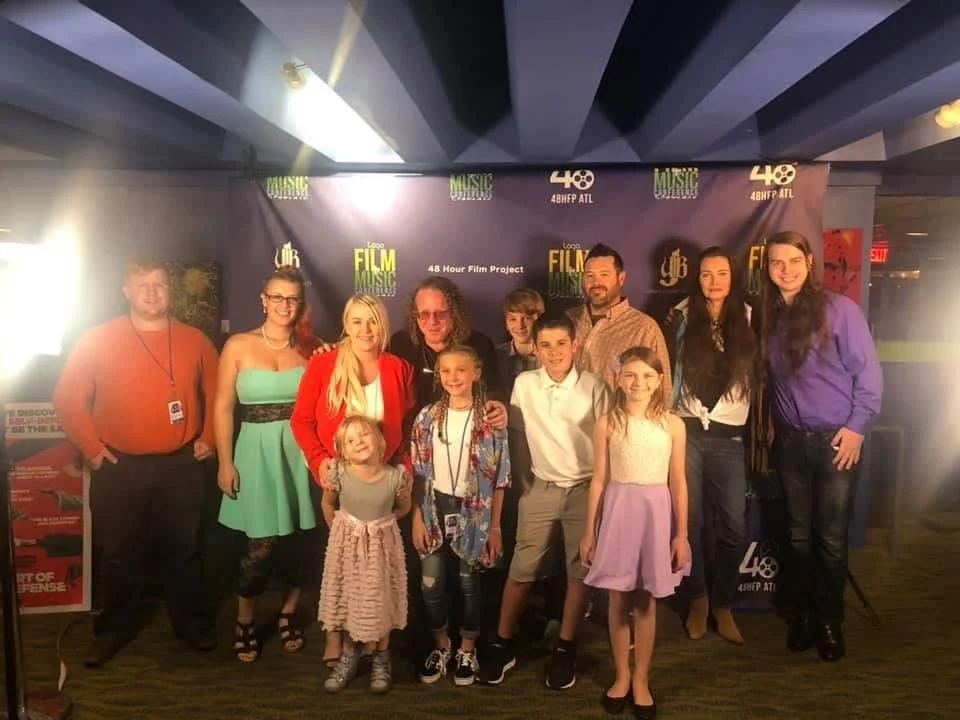 A group of adults and children posing in front of a backdrop at a film festival event.