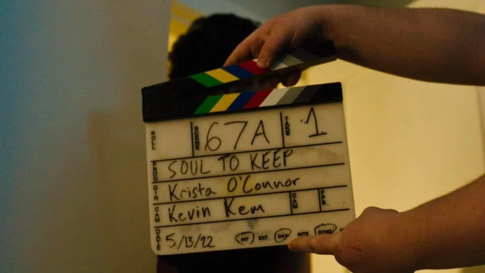 A person holding a film clapperboard with handwritten details including the title 'SOUL TO KEEP', names Krista O'Connor and Kevin Kern, and the date 5/13/22.