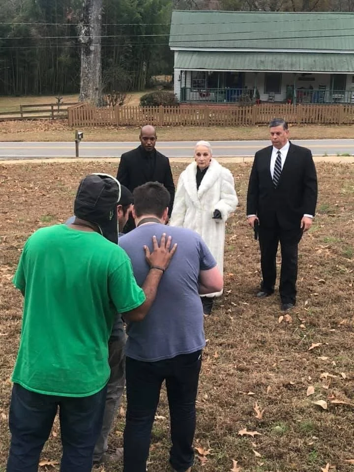 People praying outside near a road with a house in the background.