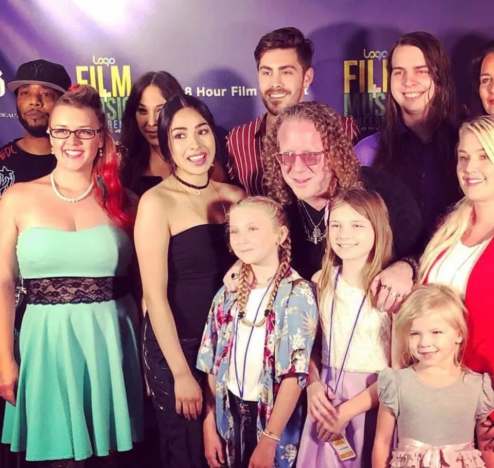Group of people at an event, with a backdrop mentioning 'Film Music' and '8 Hour Film'. Everyone is smiling and posing for the photo.