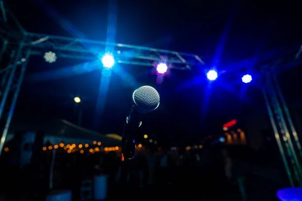 A microphone on a stage with colorful lights illuminating the background at a nighttime outdoor event.