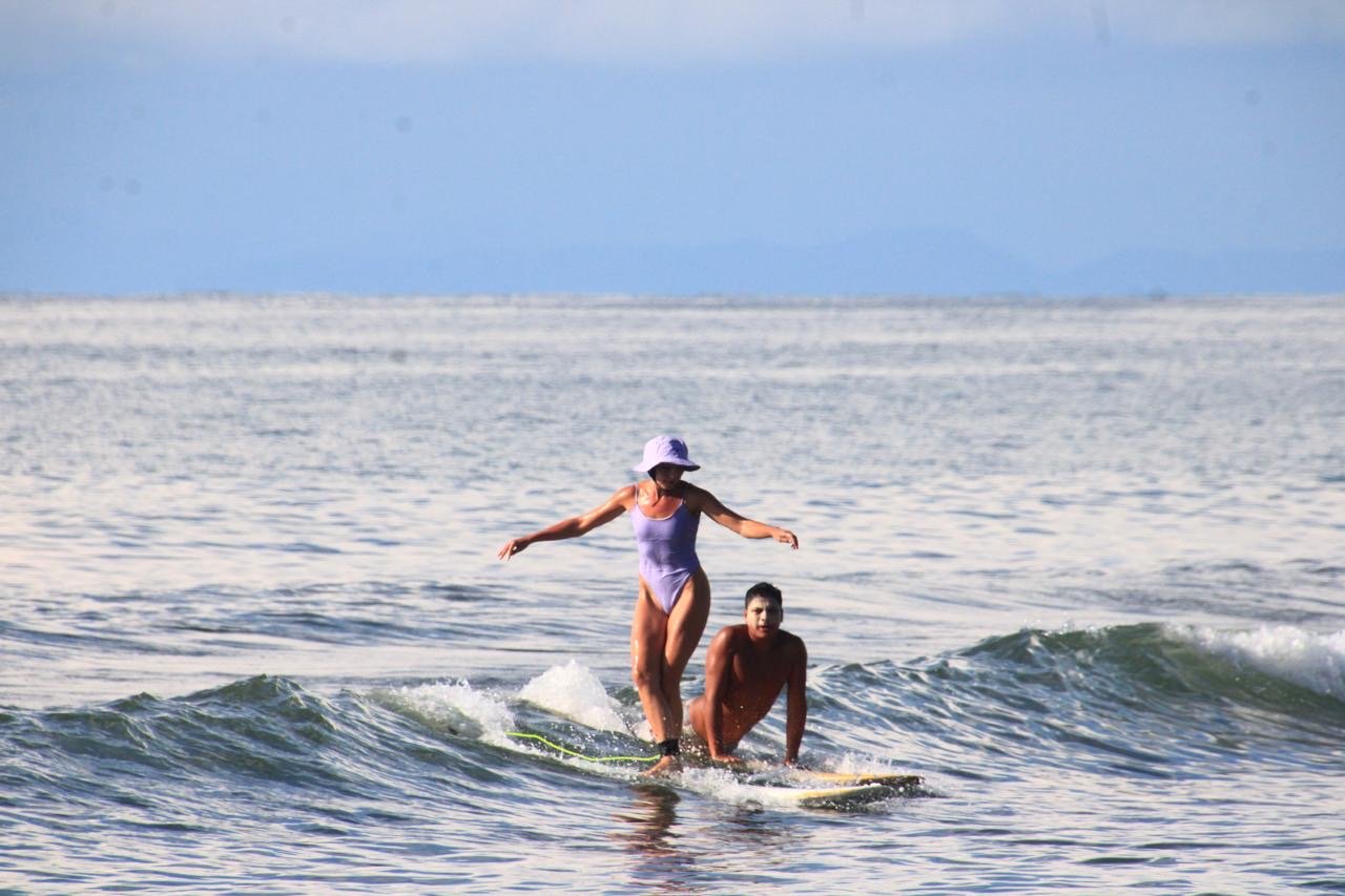 A woman and a man surfing on the ocean, with the woman standing on the surfboard and the man kneeling behind her.