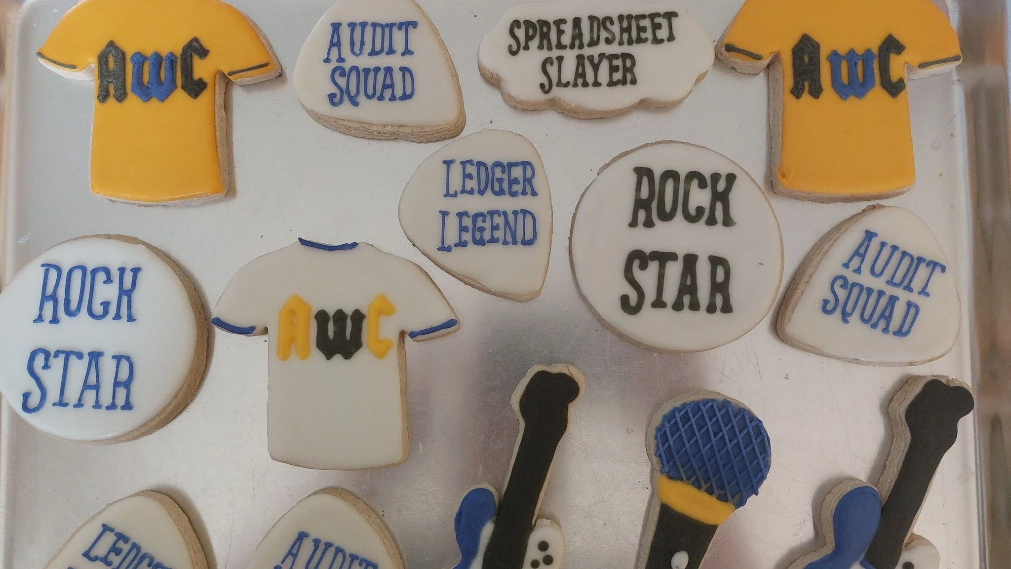 Cookies decorated with themes related to rockstars, including words like 'AwC', 'Audit Squad', 'Spreadsheet Slayer', and ' Ledger Legend', as well as microphones and electric guitars