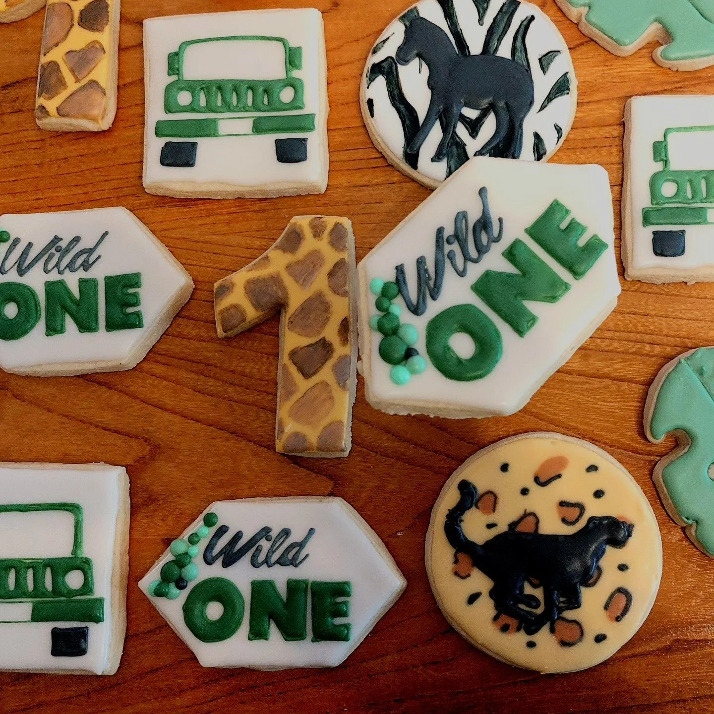Decorated cookies with wild animal themes including a giraffe, jungle scene with leopard print, and a black horse, placed on a wooden surface.