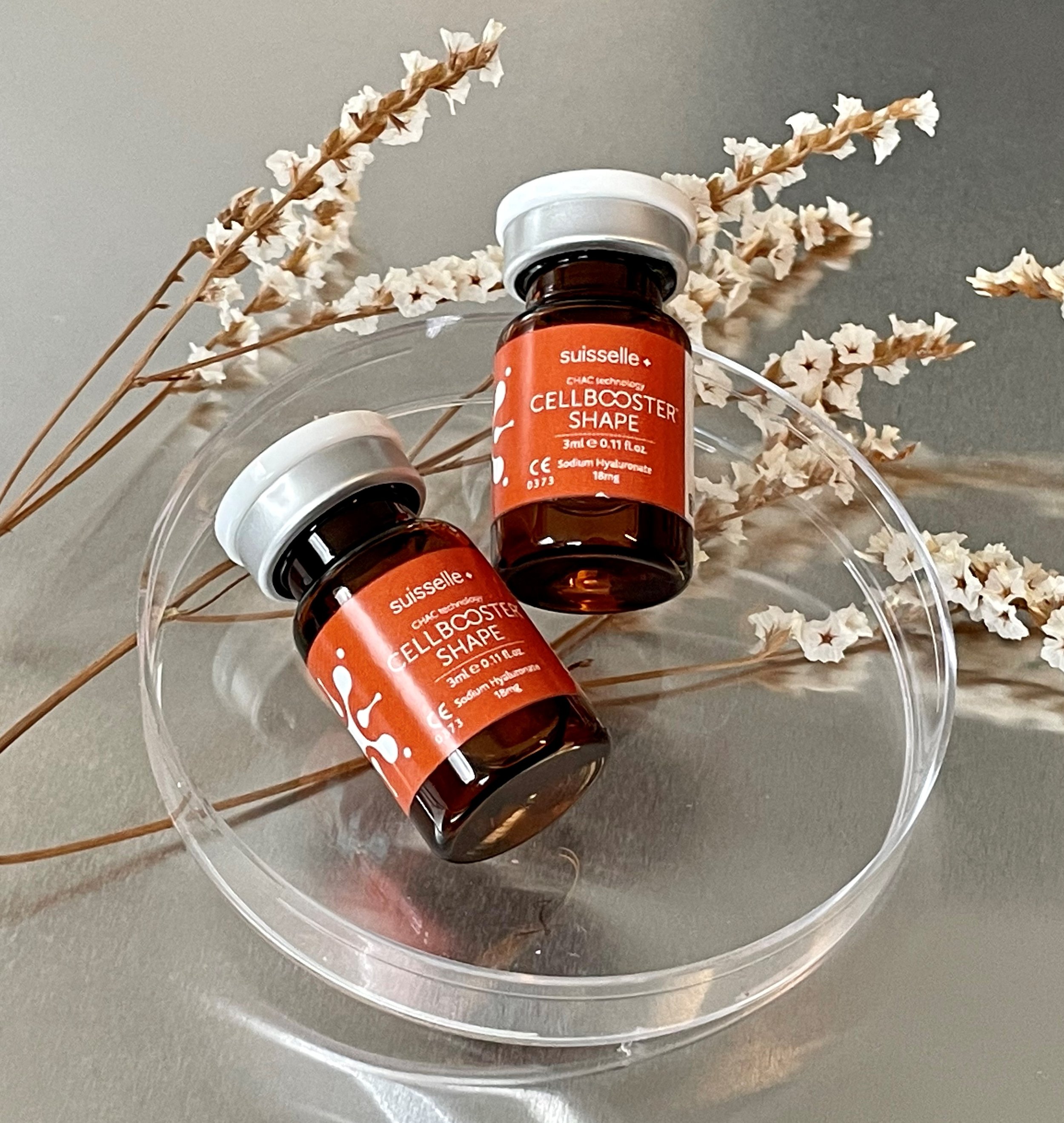Säilöntäainepullo, jossa lukee 'CELLBOOSTER SHAPE', pöydällä koristeena kuivattuja siemenkukkia.