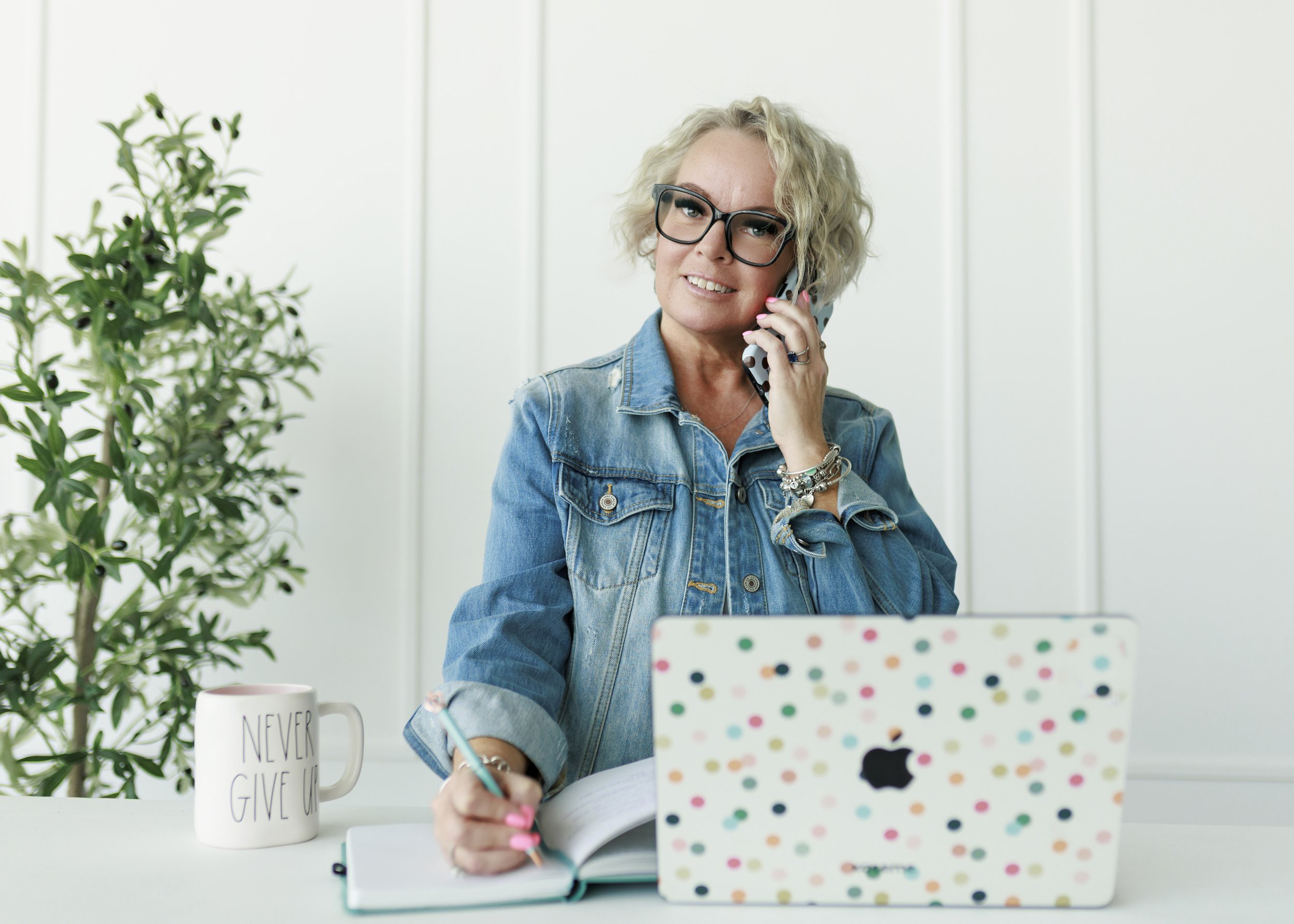 woman in denim jacket on phone with polka dot case MacBook with polka dot case journal and pen rae Dunn mug never give up black gucci glasses blonde hair