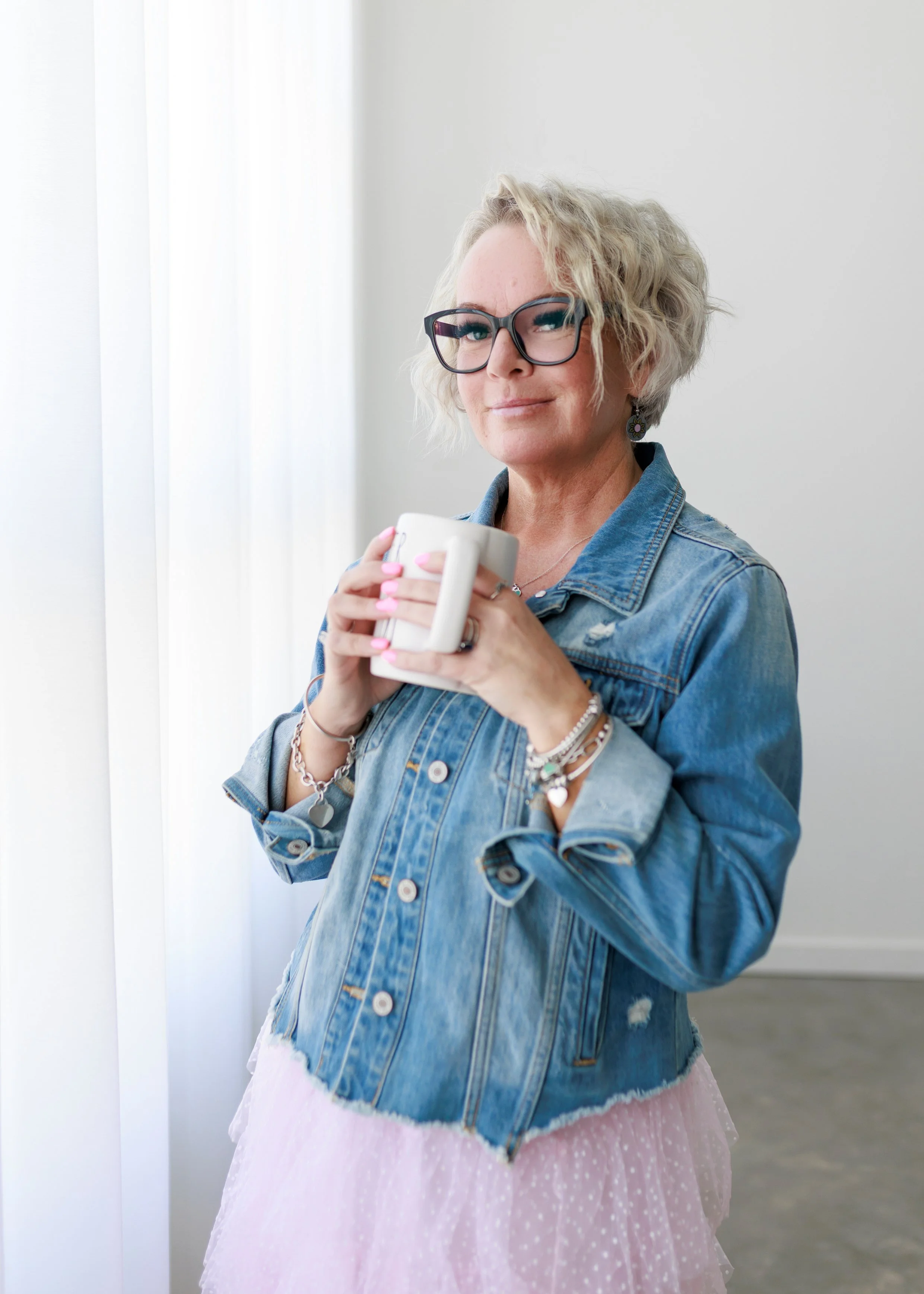 woman wearing pink tulle skirt and denim jacket wearing black glasses and blonde hair are Dunn mug never give up pink nails Tiffany necklace