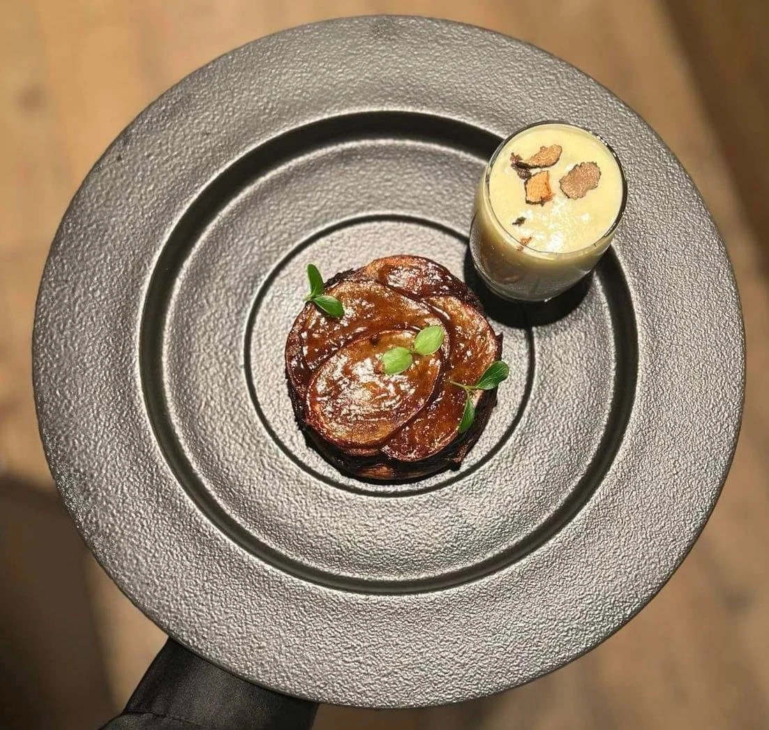 Assiette avec une portion de saucisses de pommes de terre accompagnée d'une petite coupe de crème ou de mousse garnie de copeaux de truffe.