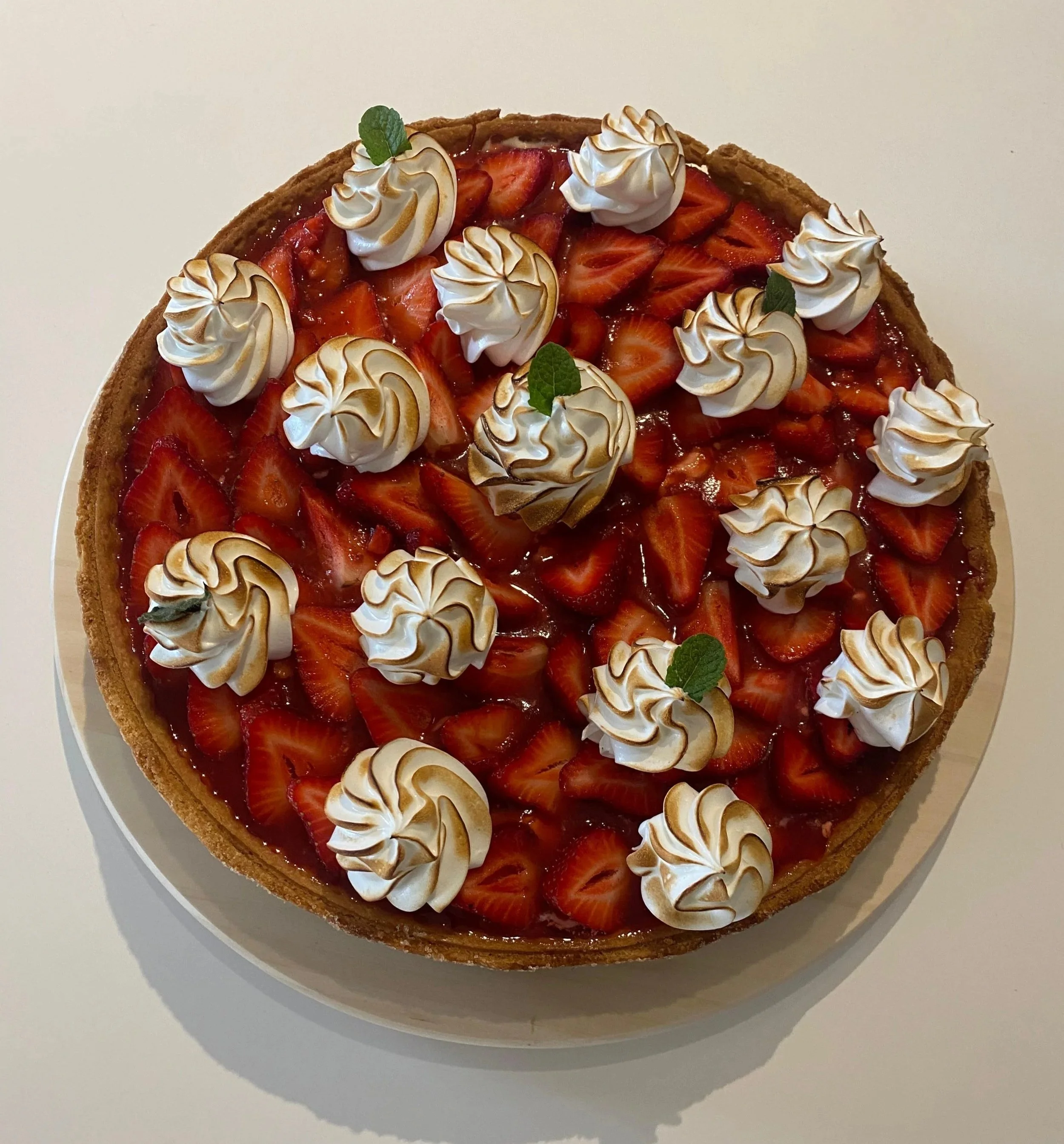 Gâteau aux fraises avec des décorations de crème meringuée et des feuilles de menthe, vue de dessus sur un plat blanc.