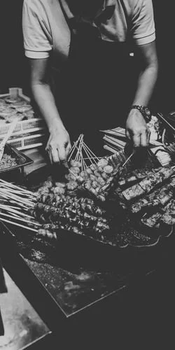 Une personne prépare des brochettes de viande et de légumes sur un barbecue.