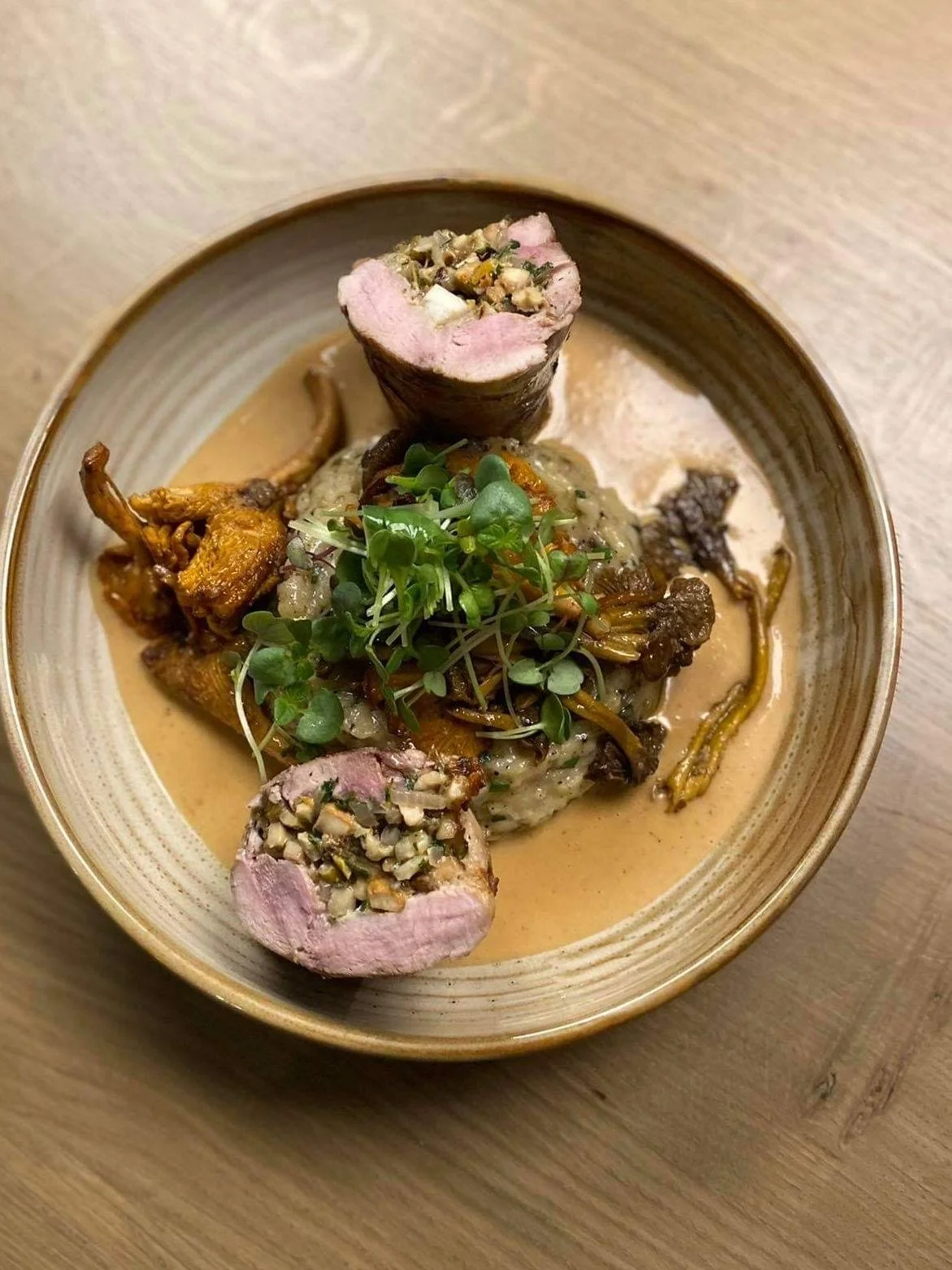 Plat gourmet avec morceaux de viande enrobés d'algues, garnis de pousses vertes, dans une sauce crémeuse, servi dans un bol en céramique sur une table en bois.