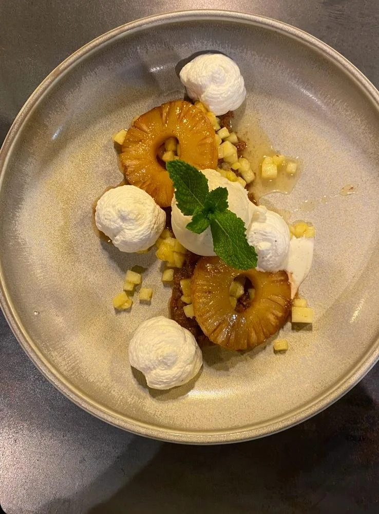 Dessert avec tranches d'ananas, boules de sorbet ou glace, cubes de fruit ou biscuit, et une feuille de menthe sur une assiette