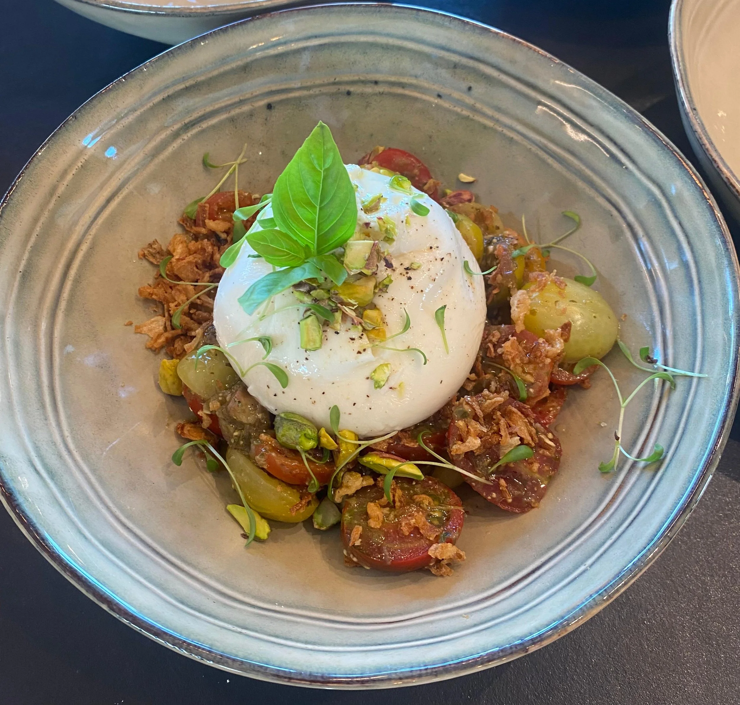 Une assiette contenant des tomates cerises, de la viande, un œuf poché, des microgreens et des graines, présentée dans un bol en céramique.