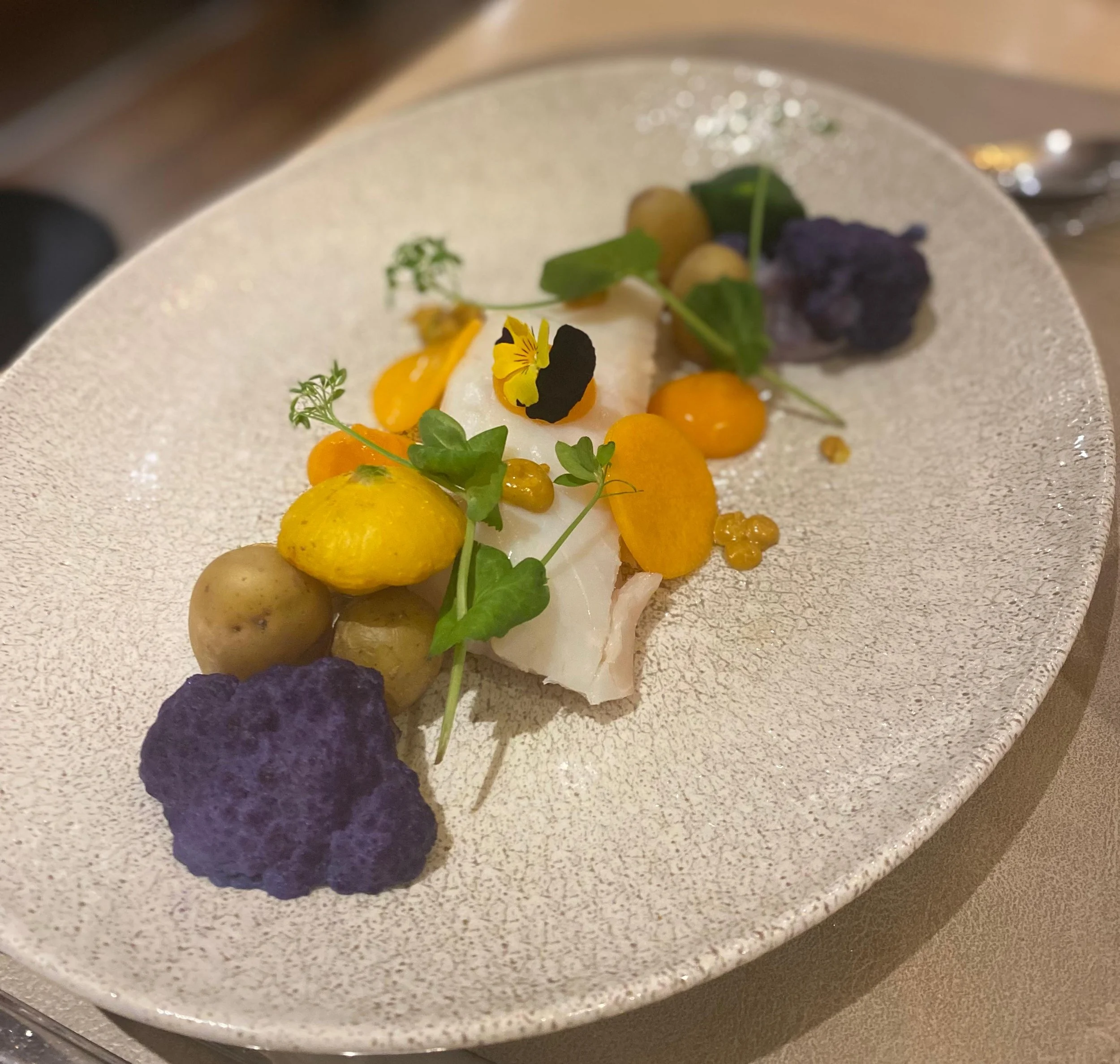 Dessin gastronomique avec quelques éléments végétaux, décorations et produits alimentaires colorés, présenté dans une assiette blanche à texture ardoise.