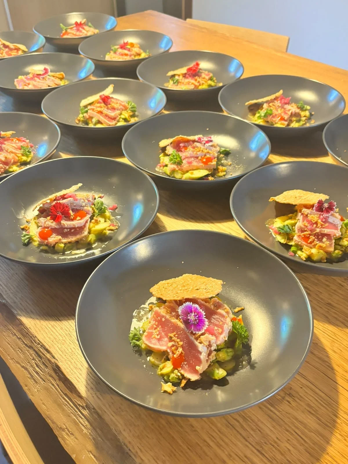 Assiettes de sashimi de thon cru avec décoration florale, servies sur une table en bois.