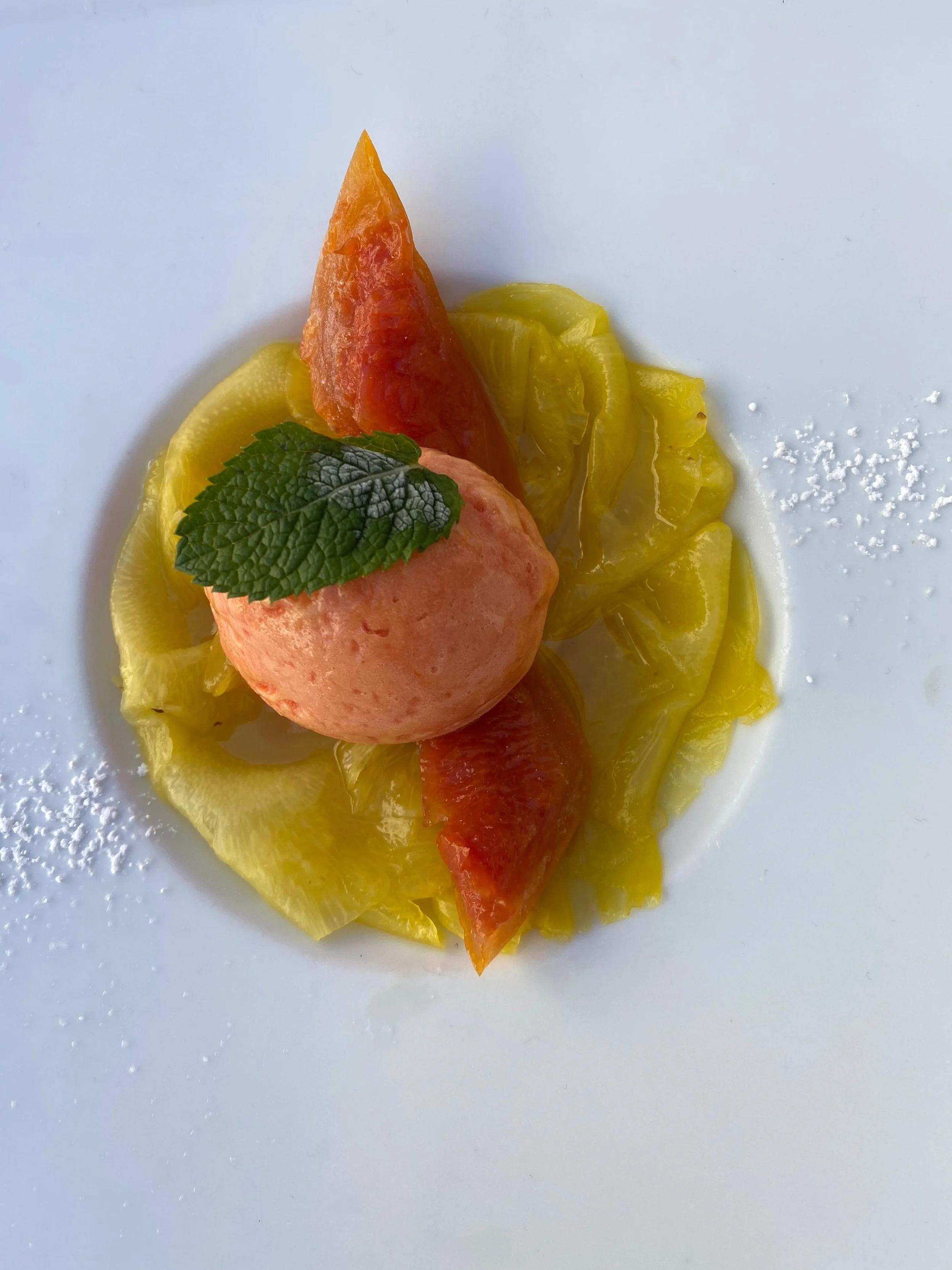 Dessert avec une boule de sorbet à la pêche, une tranche de melon, une tranche de pastèque, une feuille de menthe et une fine couche de sucre glace sur une assiette blanche