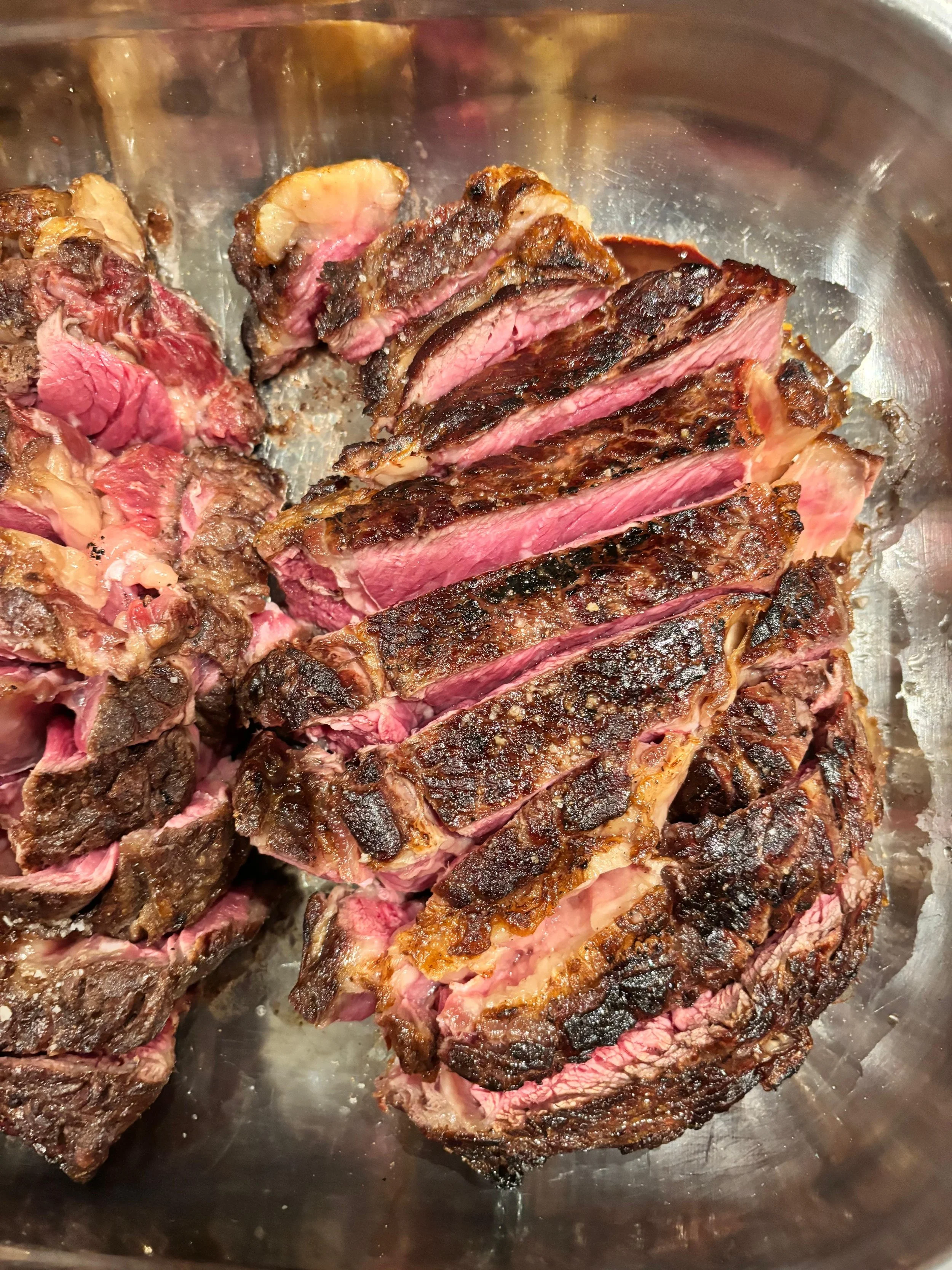 Gros plan d'une pièce de steak cuite à point, marinée avec une croûte grillée, dans un bol en inox.