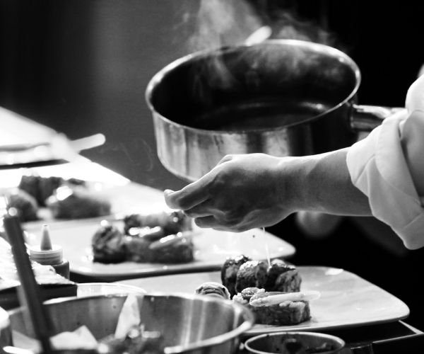 Chef en train de verser de la vapeur sur des plats préparés dans une cuisine professionnelle.