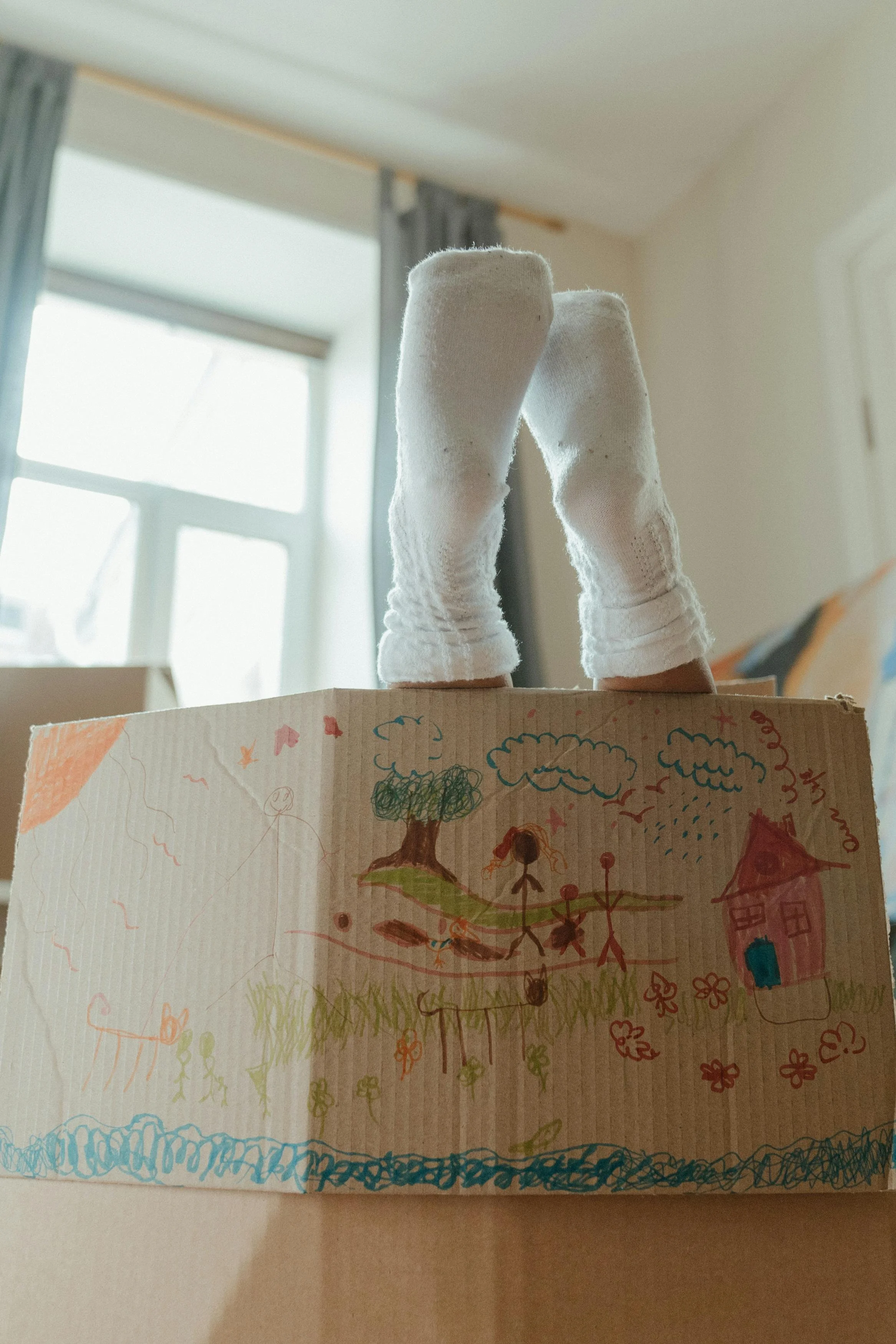 A child's drawing on a piece of paper, showing trees, a house, flowers, and a person, with colorful crayon sketches.