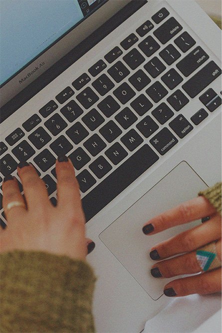 A person's hands with black nail polish typing on a silver MacBook Air keyboard.